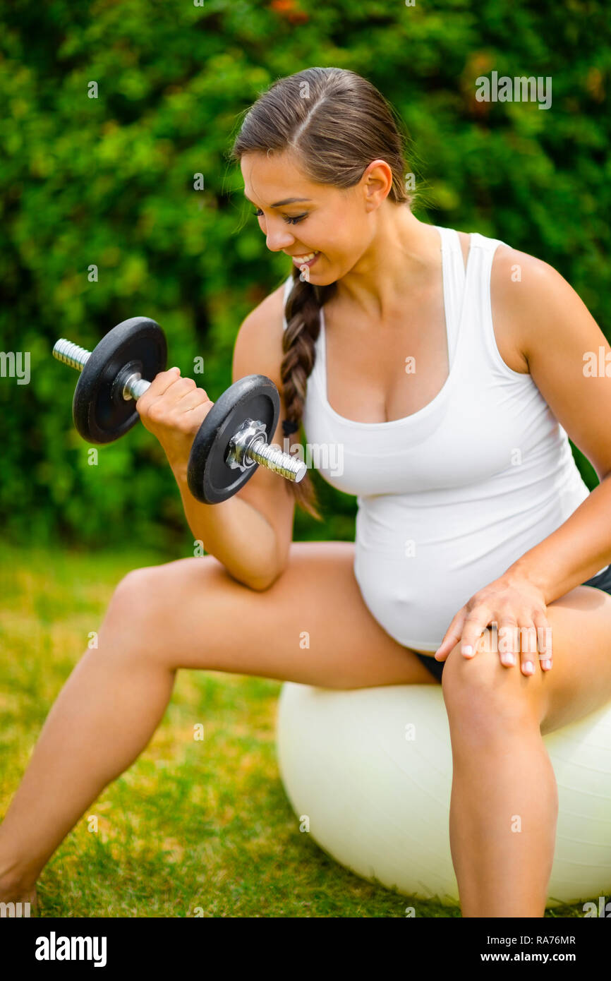 Pregnant Woman Smiling While Lifting Weights On Exercise Ball Stock Photo