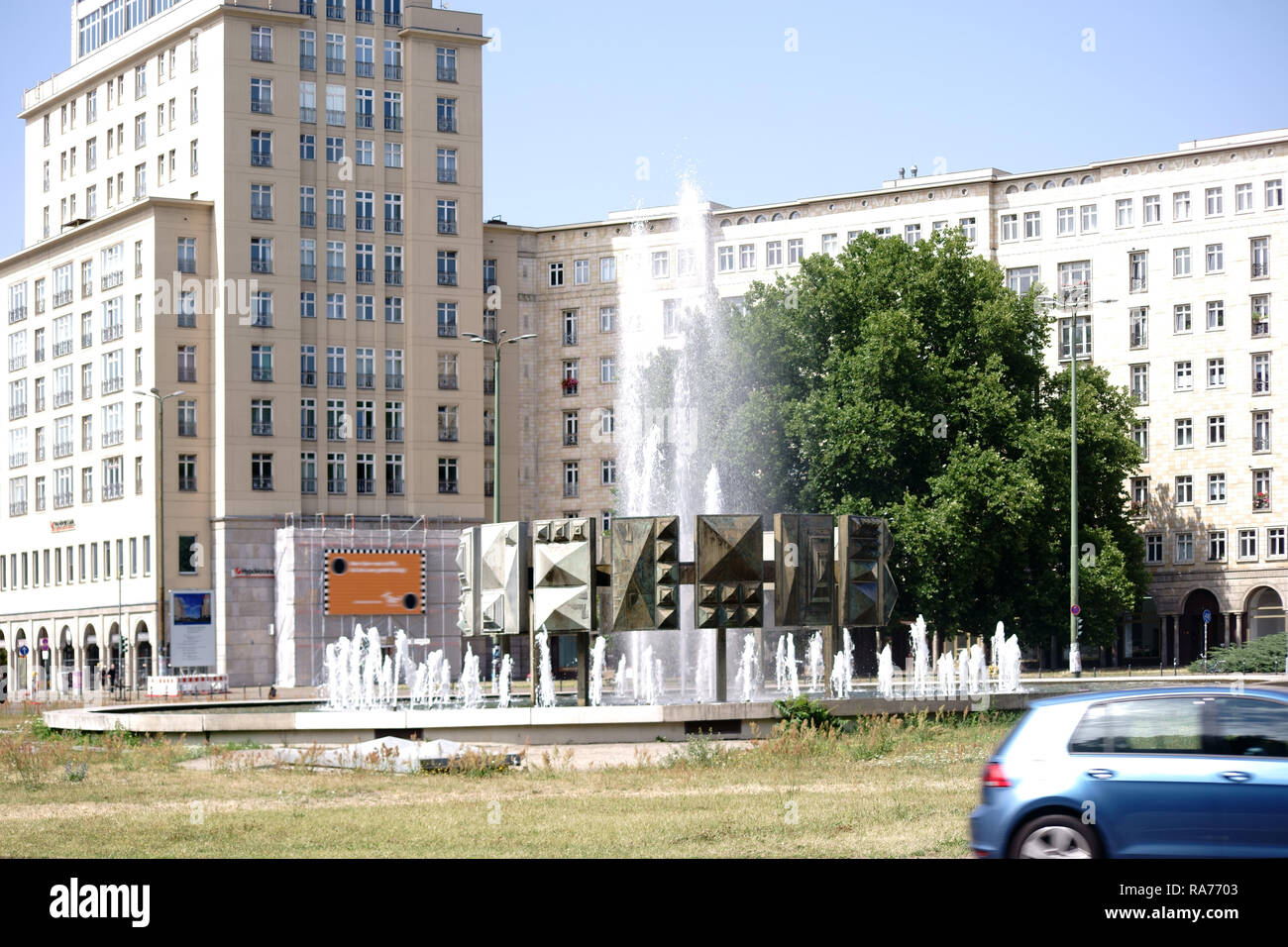 The water of the fountain Schwebender Ring on the Strausberger Square and at Karl-Marx-Alley with roundabout traffic in Berlin. Stock Photo