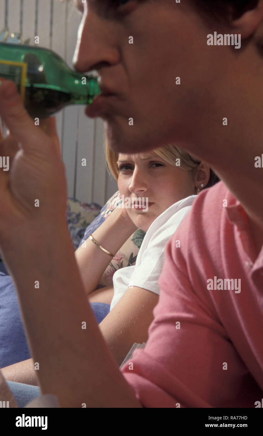 young woman looking daggers at her partner who is drinking beer Stock Photo
