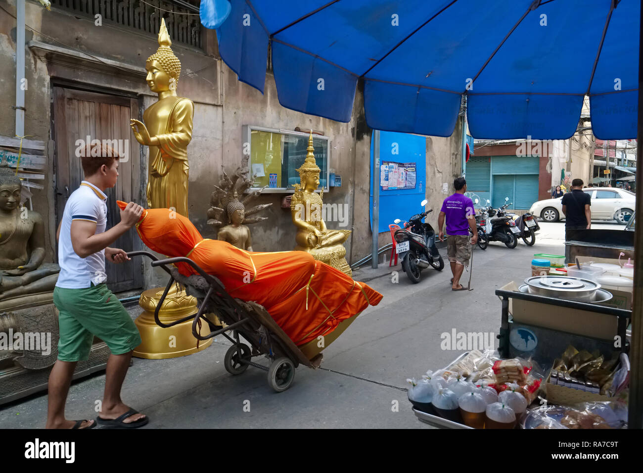 An employee of a factory for Buddha statues rolls out a new Buddha, respectfully wrapped in orange cloth; Bamrung Muang Road, Bangkok, Thailand Stock Photo