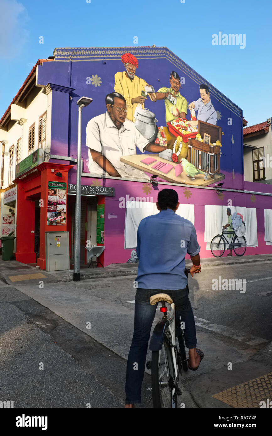 A cyclist in Little India, Singapore, looks at a wall painting depicting professions of early Indian immigrants, such as a washerman with his bicycle Stock Photo