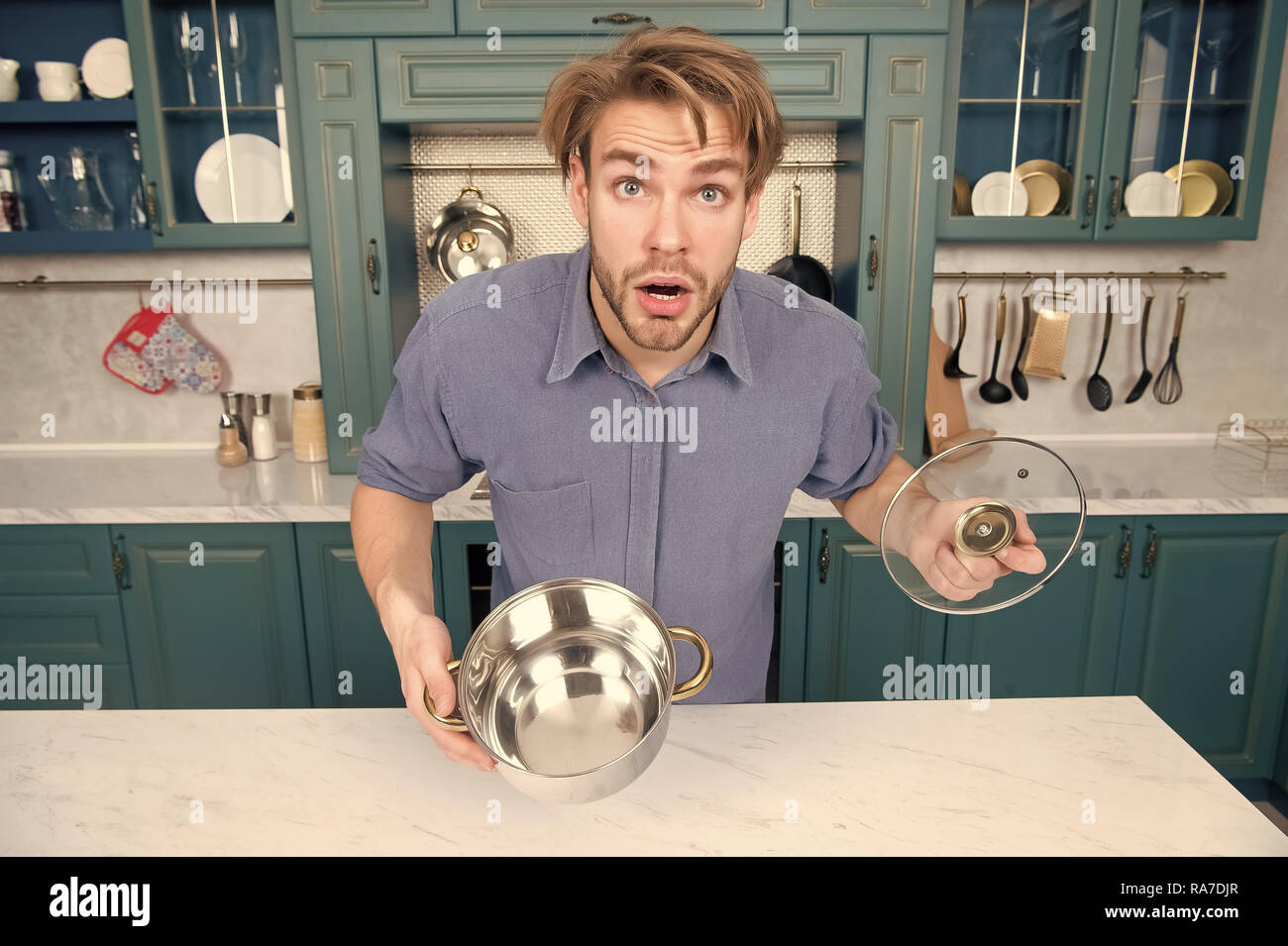 Guy with surprised face hold open saucepan, lid in kitchen. Man with