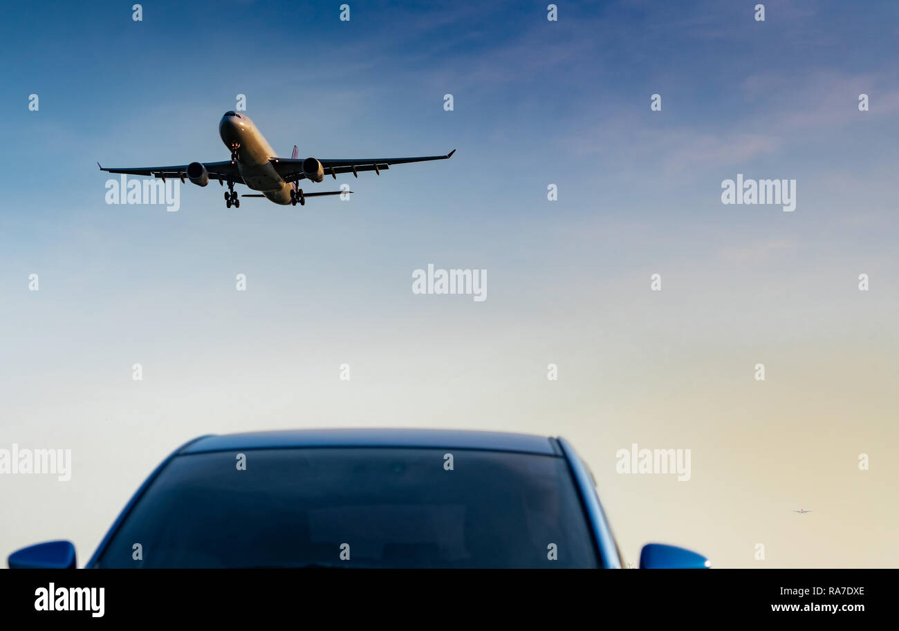 Commercial airline. Passenger plane landing approach blue SUV car at airport with blue sky and clouds at sunset. Arrival flight. Vacation time. Happy  Stock Photo