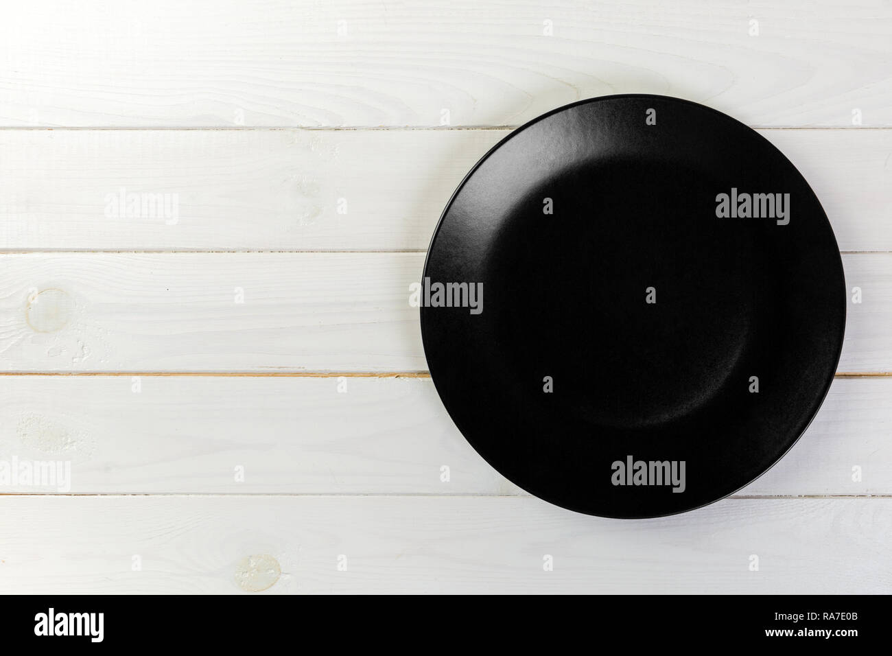 Directy above Empty black matte plate on white wooden background with ...