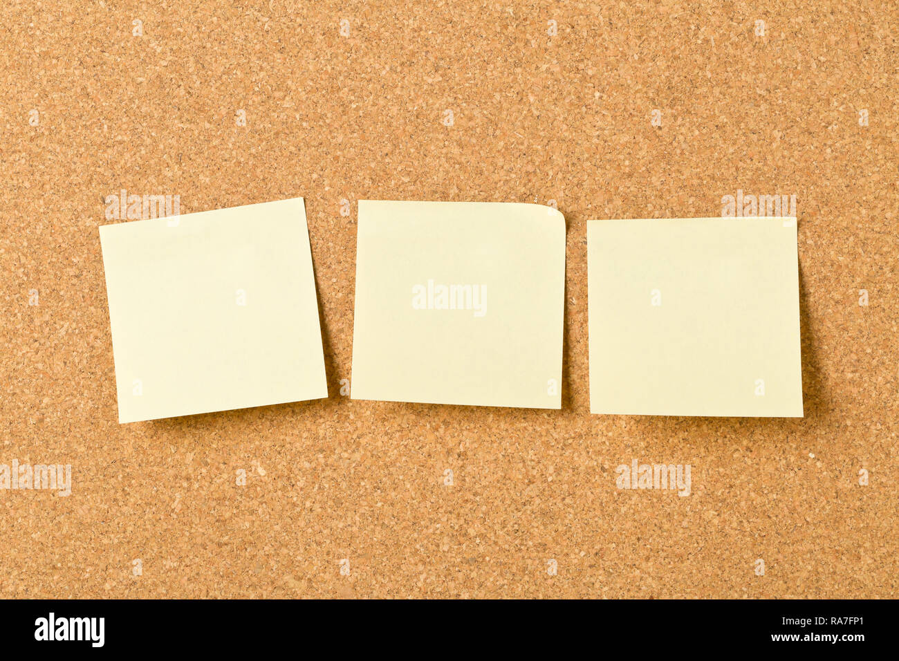 Three empty yellow sticky paper memo notes on cork board with copy space Stock Photo