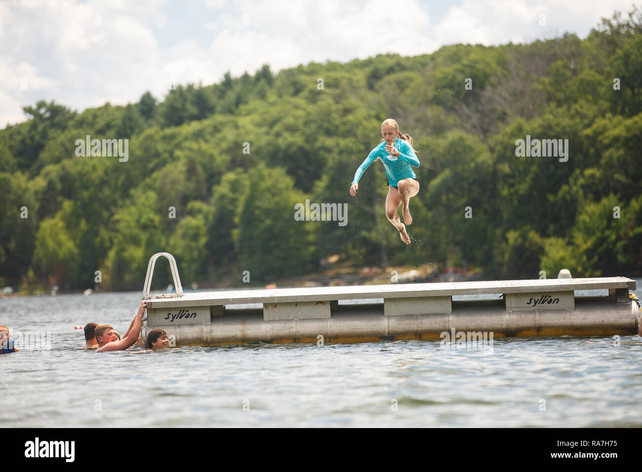 A young girl jumps off of a raft floating in the middle of a lake at a summer camp Stock Photo