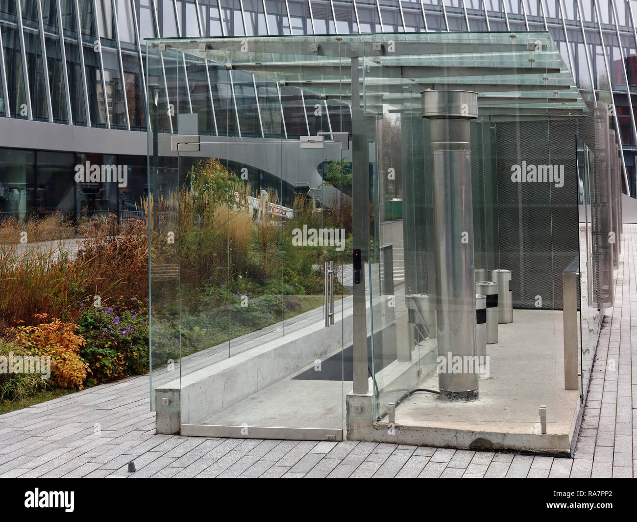 The smoking area near the modern office building is covered with glass