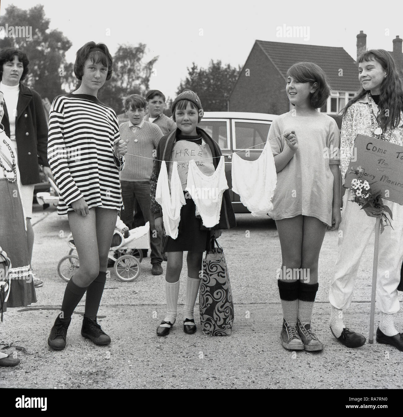 1967. Prestwood village charity fete, local girls selling old clothes...two  girls hold a piece of string with their grannies old underwear on, while a  girl in te middle has a sign on
