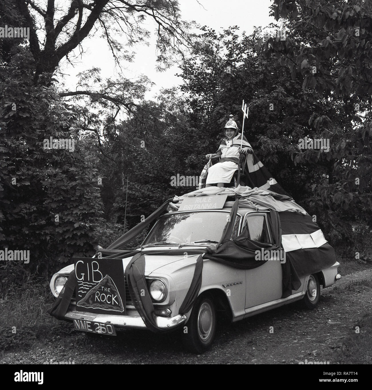 1967, Prestwood village fete, young girl in fancy dress and with a Union Jack cape sitting on a chair fixed on the top of a decorated car  with a 'Rule Britannia' sign on it, England, UK Stock Photo