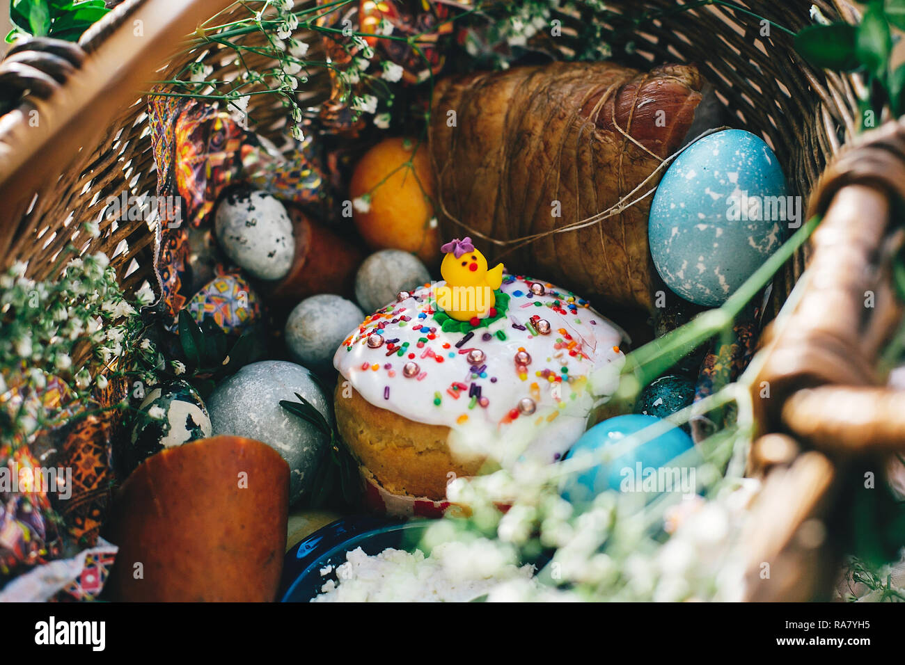 Easter basket with stylish eggs, easter bread with chicken, ham,sausage, and flowers with buxus