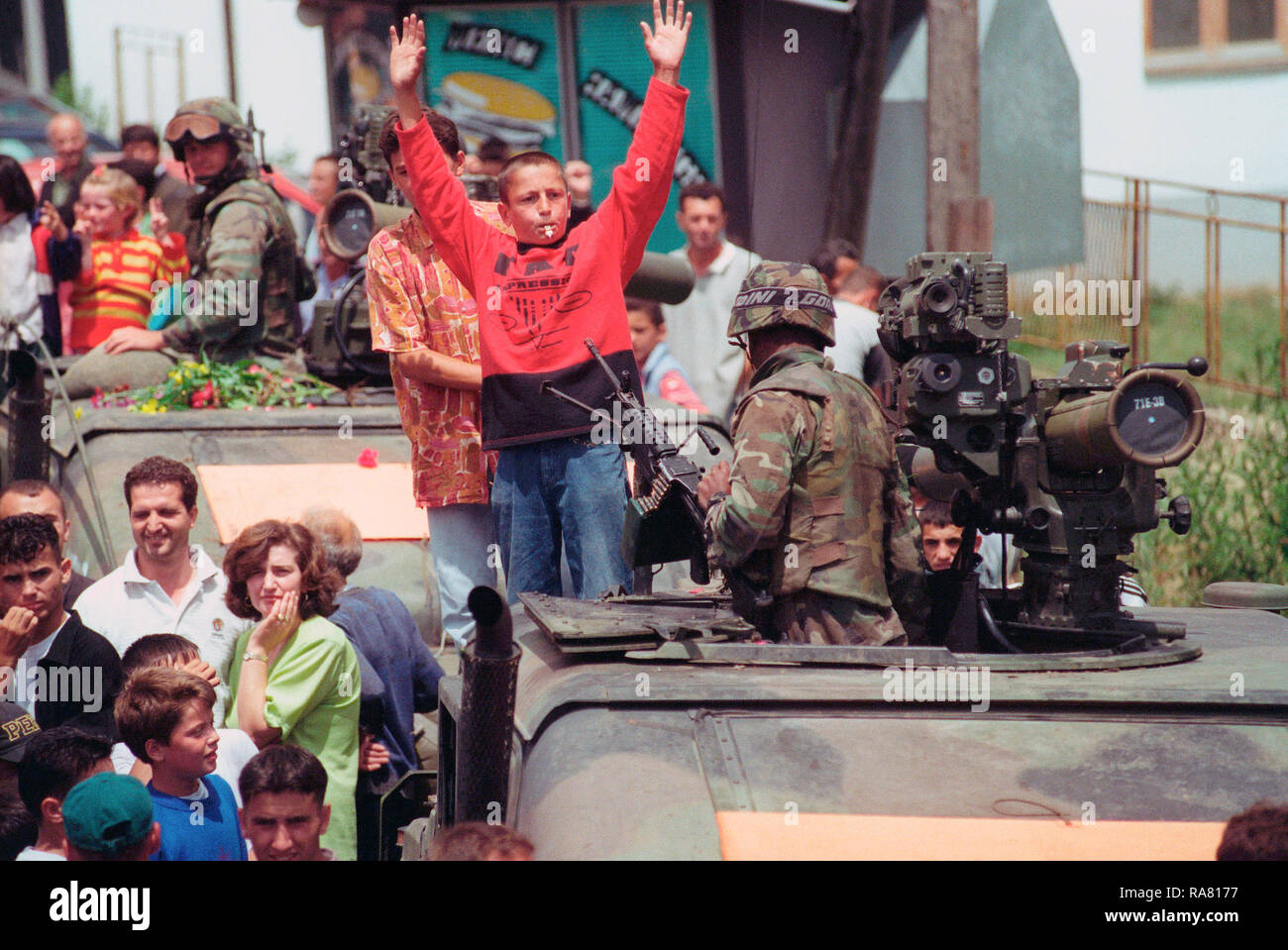 1999 - Ethenic Albanians gather in the streets for a parade held to honor American Forces in the Kosovo village of Koretin.  Kids climb on top of an M998 High-Mobility Multipurpose Wheeled Vehicle (HMMWV) with TOW missile. Stock Photo