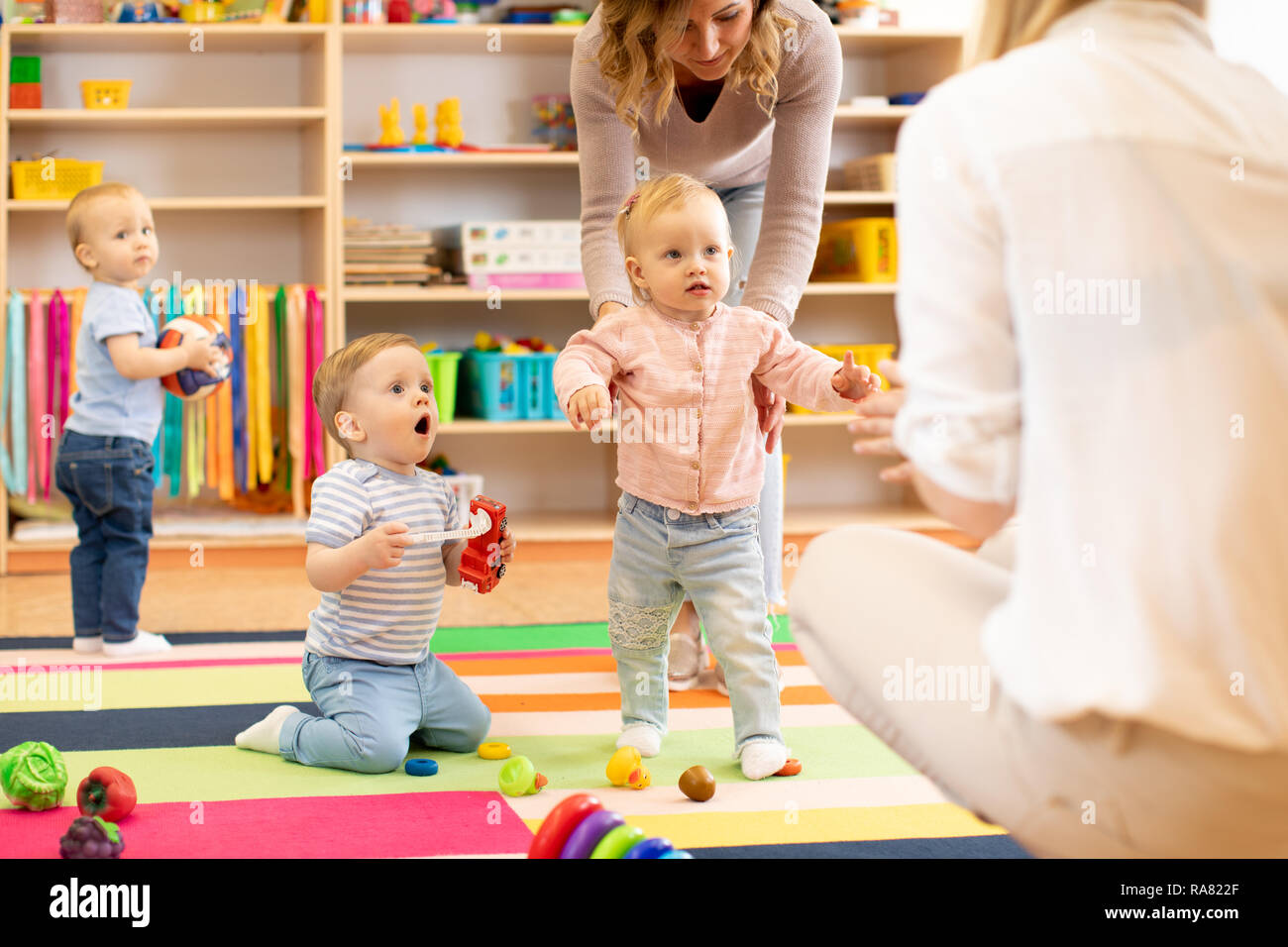 Group of workers with babies in nursery or kindergarten Stock Photo
