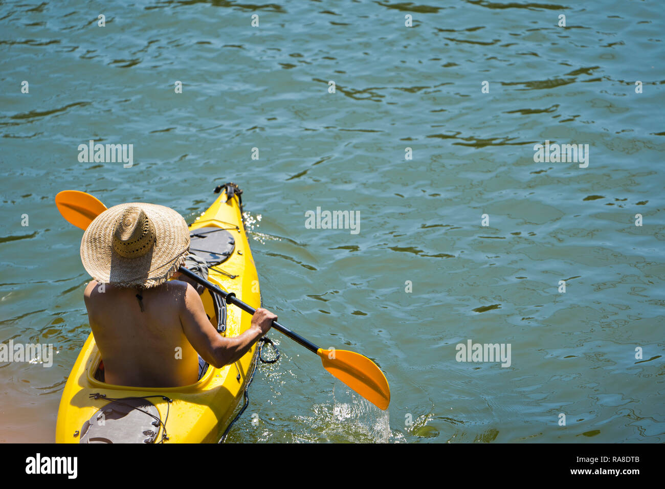 An enthusiast man with a straw hat in bathing suit are kayaking on the
