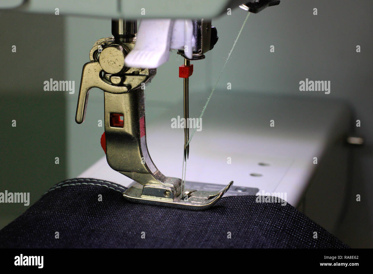 Black fabric under a pressing foot of a sewing machine with double needle. Light blue thread. Stock Photo