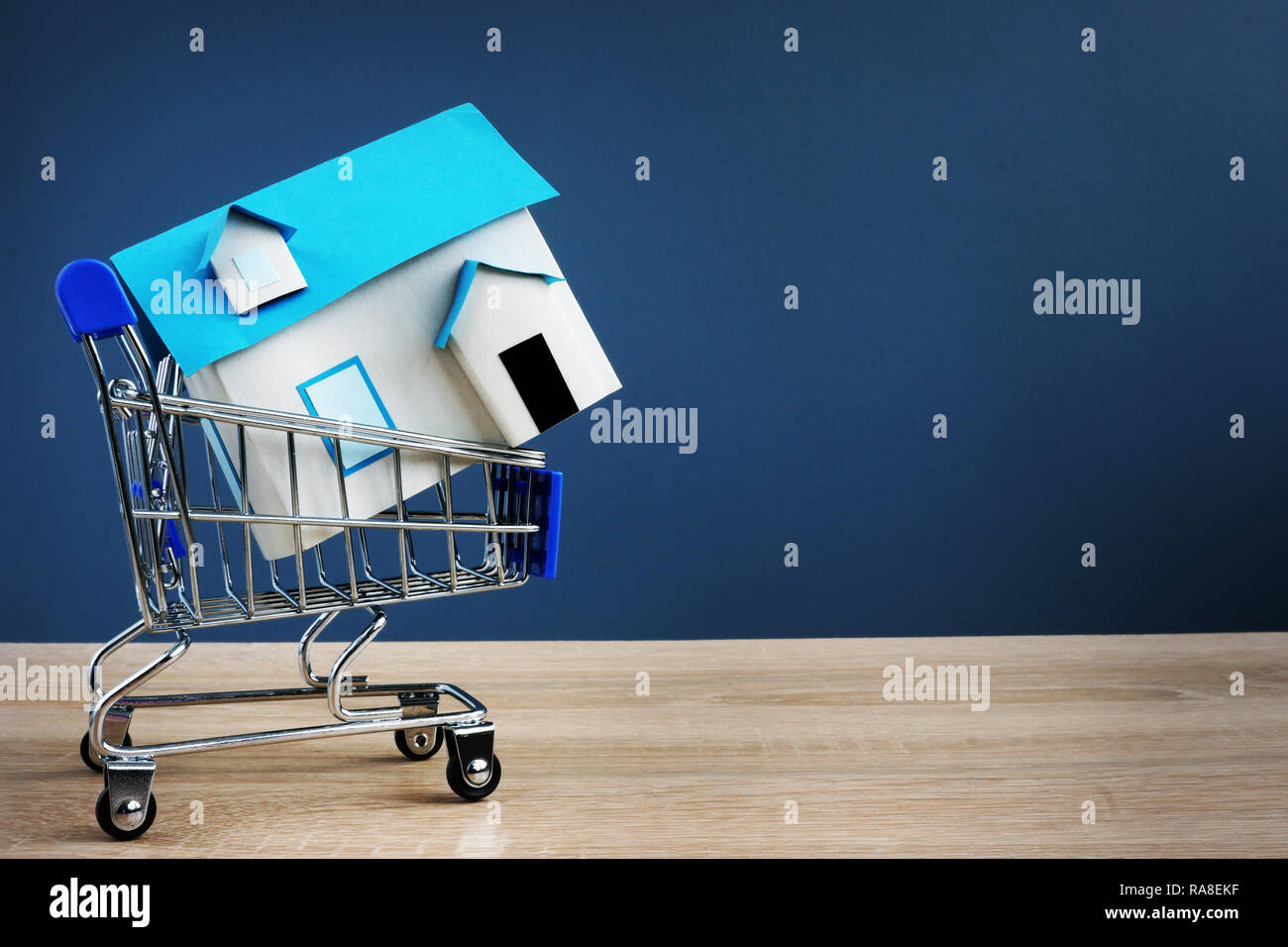 Shopping cart and small house. Buying real estate concept. Free space. Stock Photo