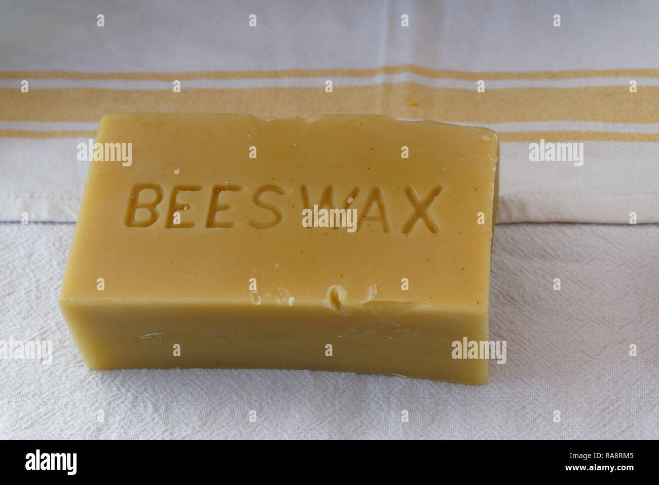 bar of golden beeswax sitting on a white kitchen towel with yellow stripes Stock Photo