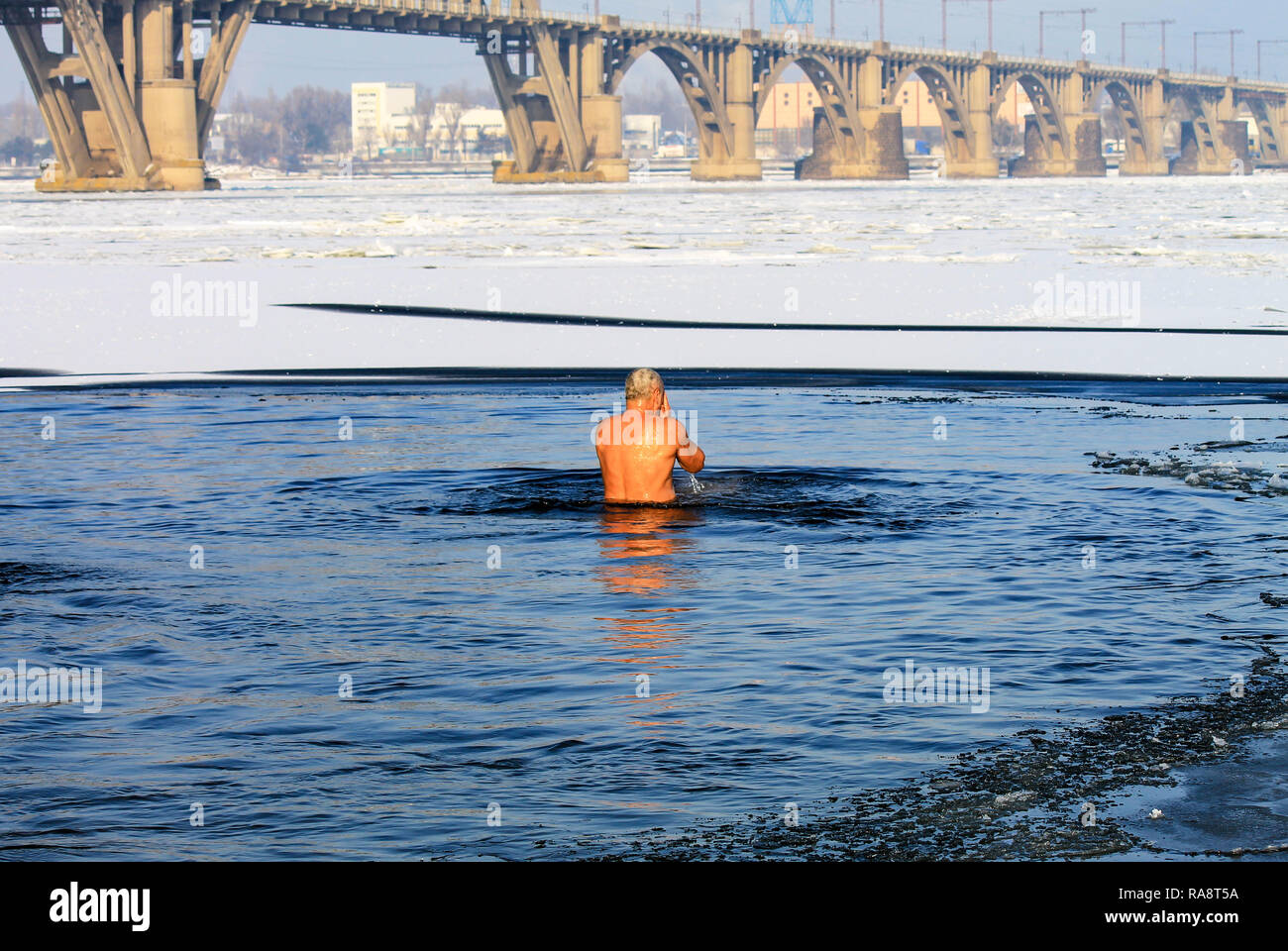Winter sport. An elderly man swims in a winter river covered with ice during the Orthodox holiday Epiphany. Hardening. Stock Photo
