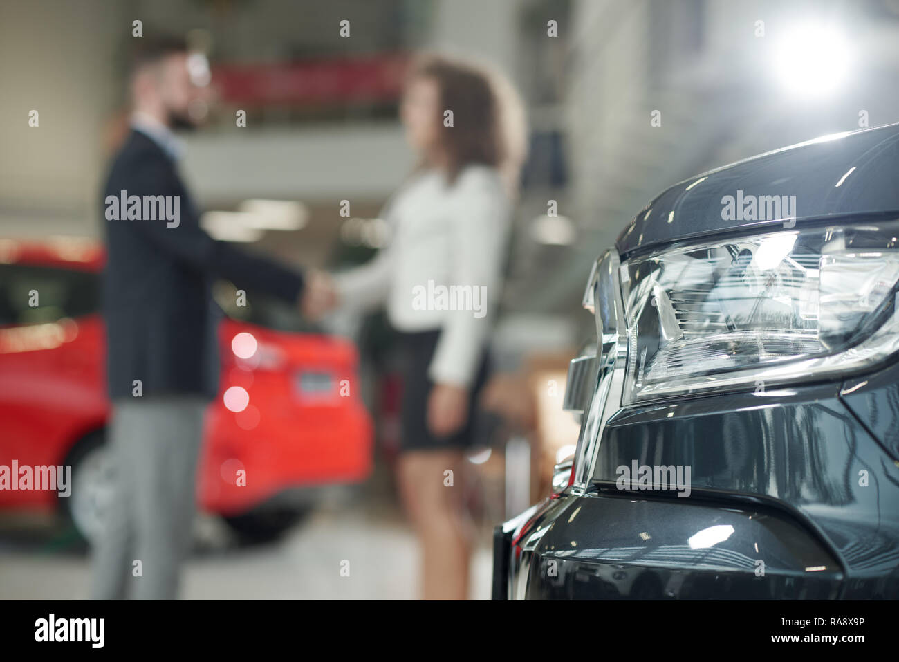 Automobile headlight. Woman and man shaking hands behind. Male manager