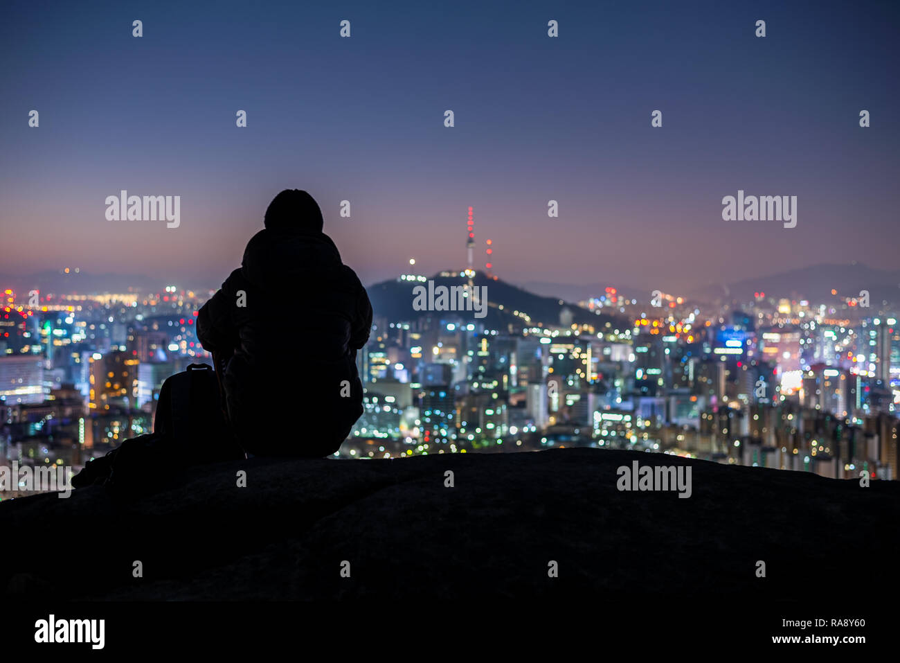 Young man traveler sitting on the rock looking Seoul city at Night,South Korea Stock Photo