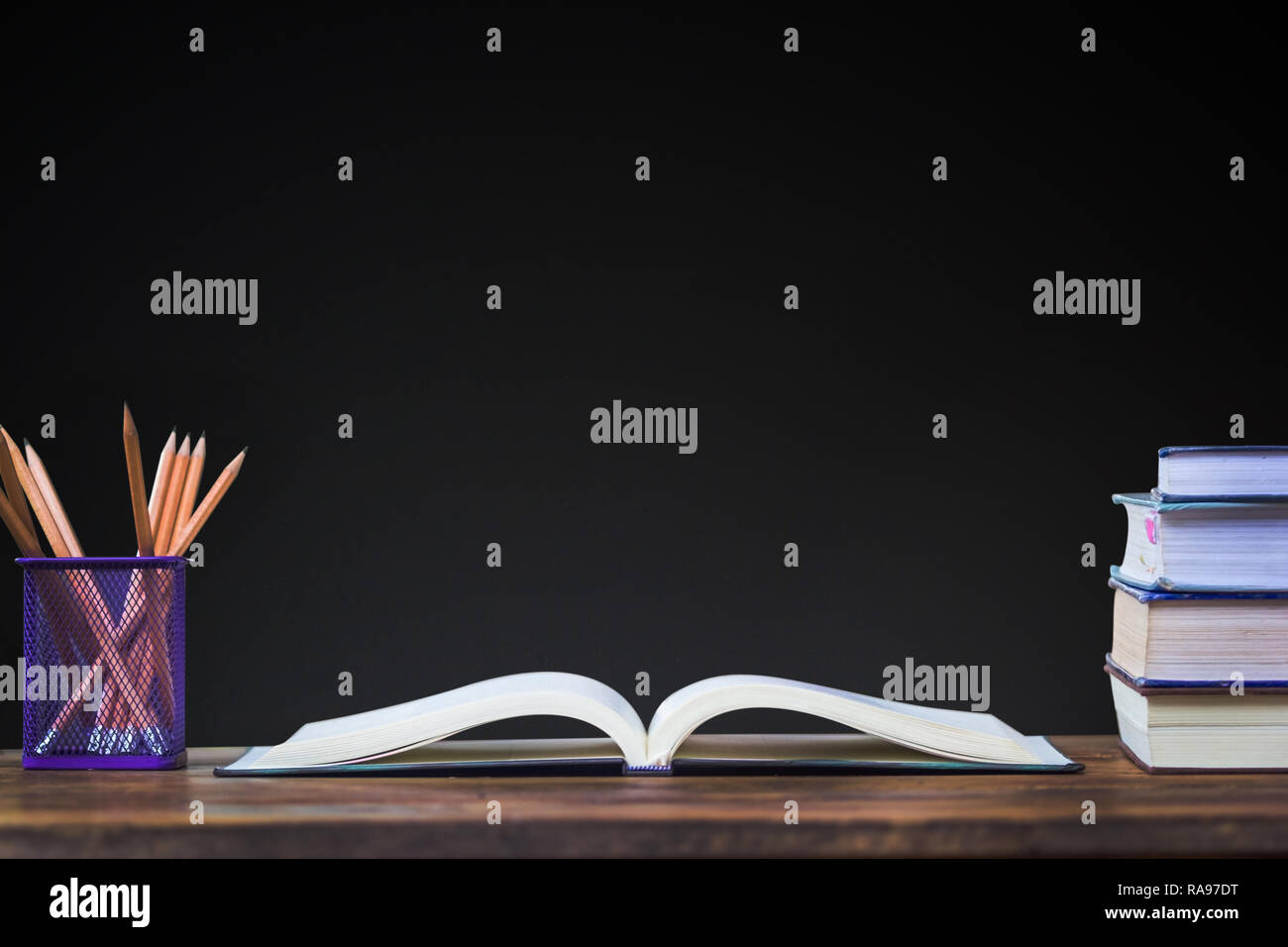 Education background concept. Opened book and pencil on wood table with black chalkboard as background. Teacher table. Stock Photo