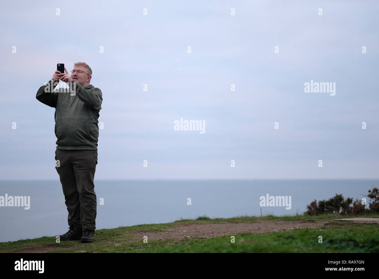 A man on a hill by the sea taking a selfie in Cornwall, UK. Stock Photo