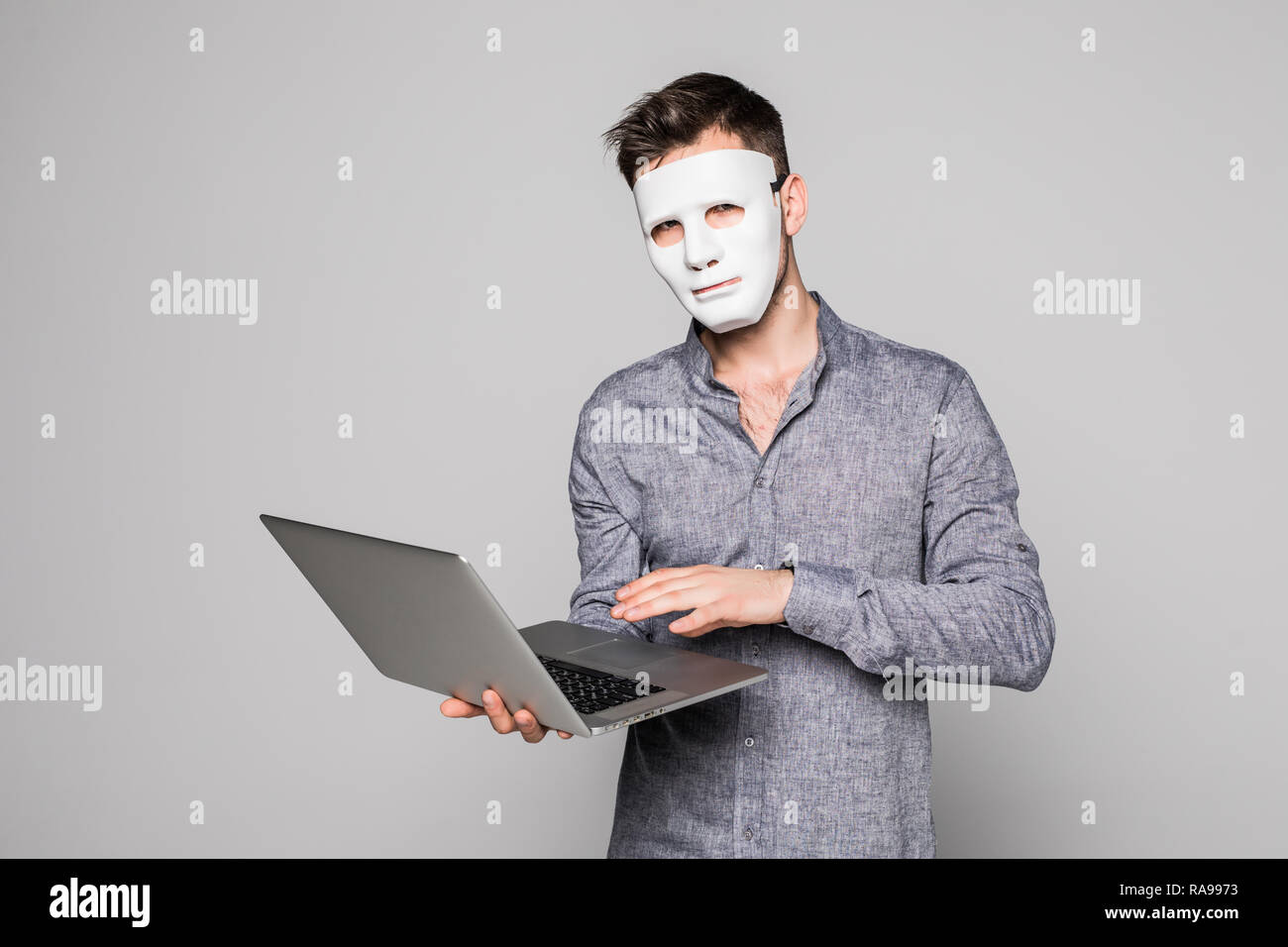 Hacker with anonymous mask with laptop while standing against white background Stock Photo