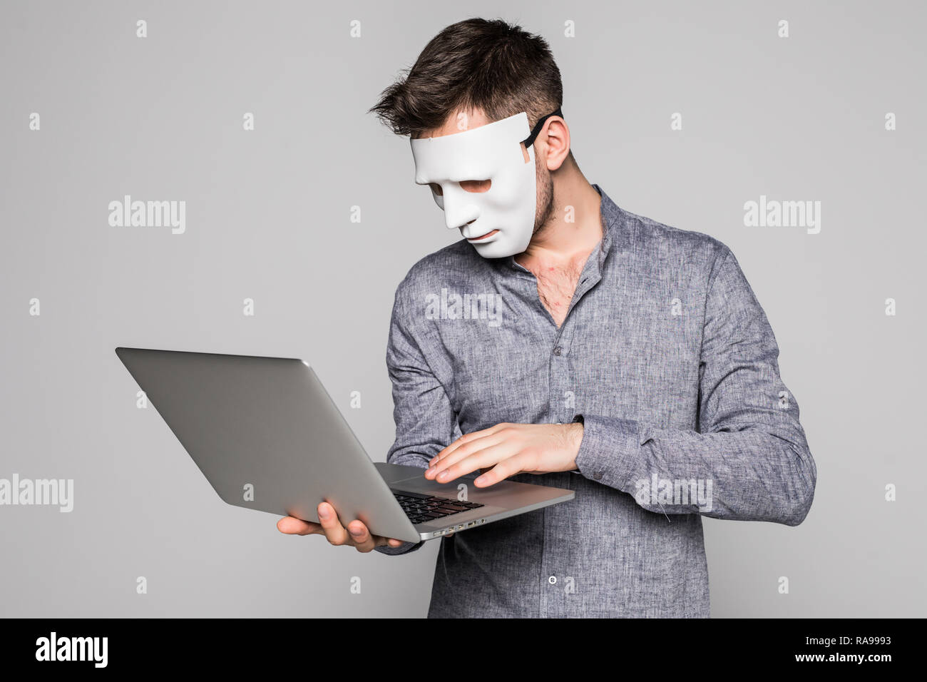 Hacker with anonymous mask with laptop while standing against white background Stock Photo
