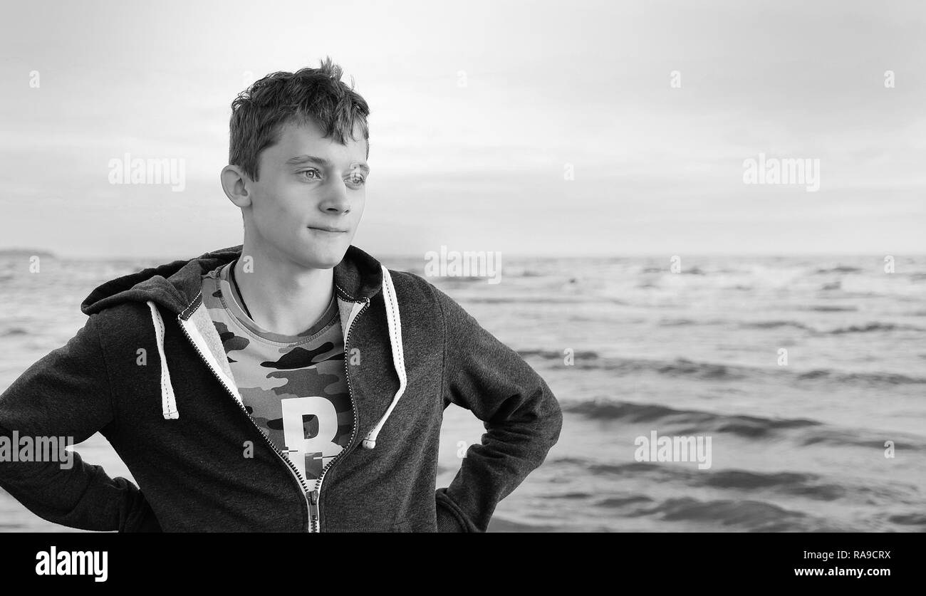 Black and white photo. Free happy young man standing on the beach feeling the warm wind looking into the distance, relaxed and carefree. Stock Photo
