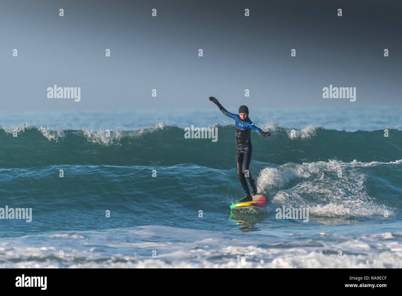 A surfer walking on a longboard surfboard on a wave at Fistral in Newquay in Cornwall. Stock Photo