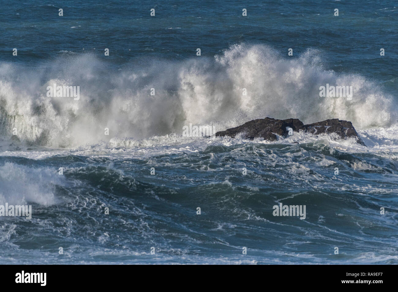 A large wave breaking on rocks in the sea. Stock Photo