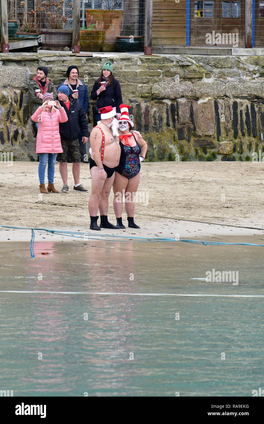 Two overweight people in swimsuits standing on the shoreline in Newquay Harbour in Newquay in Cornwall. Stock Photo