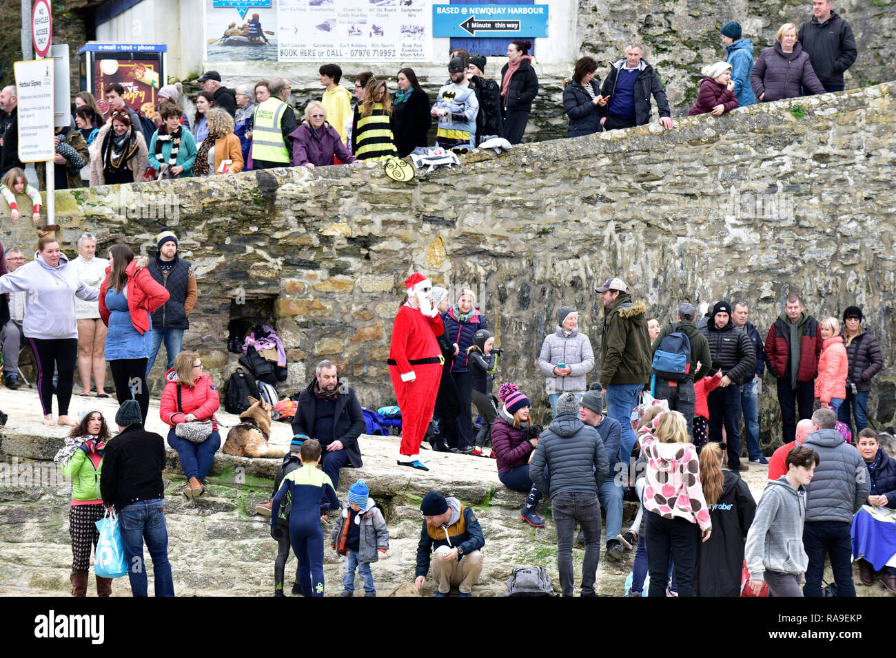 A person wearing a Santa Claus Father Christmas costume standing amongst a crowd of people on the slipway at Newquay harbour in Cornwall. Stock Photo