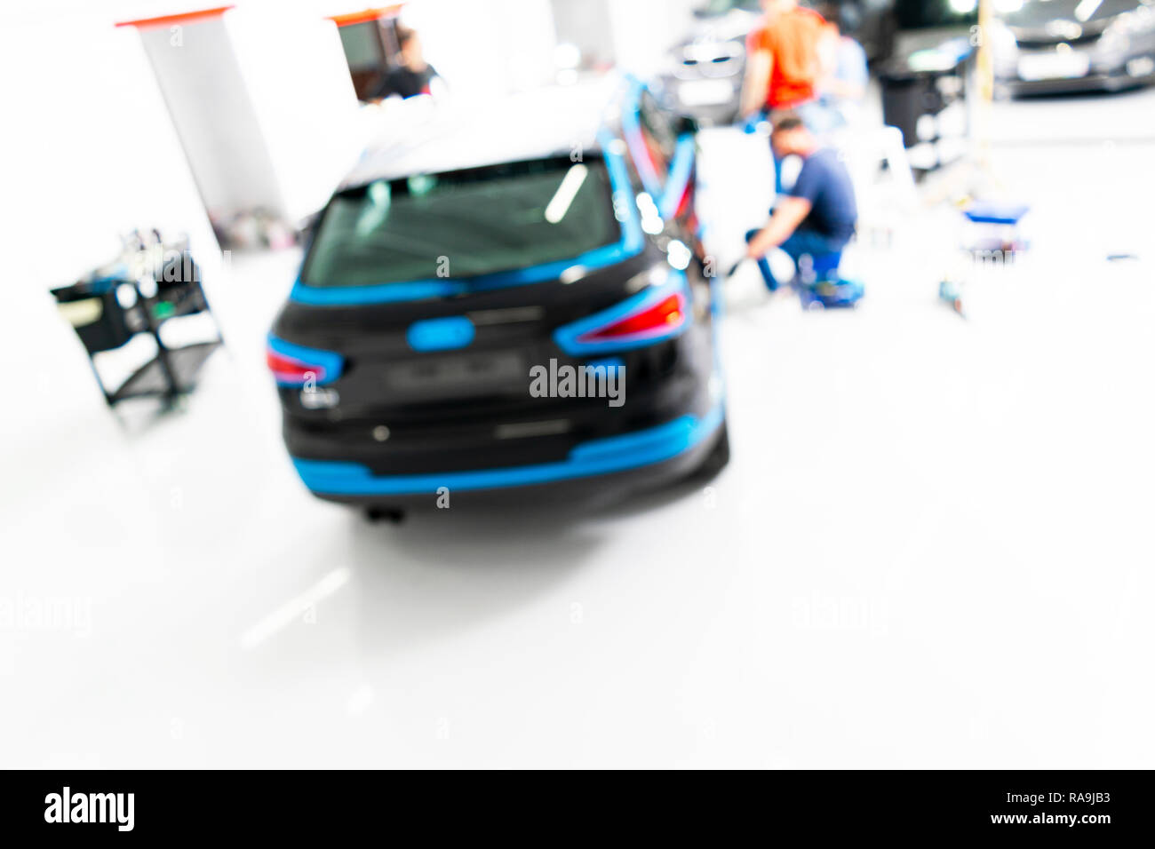 Blurred abstract image of man worker with car in body shop. Blur car auto service. Car bokeh. Blurred background with car in garage. Vehicle maintenan Stock Photo