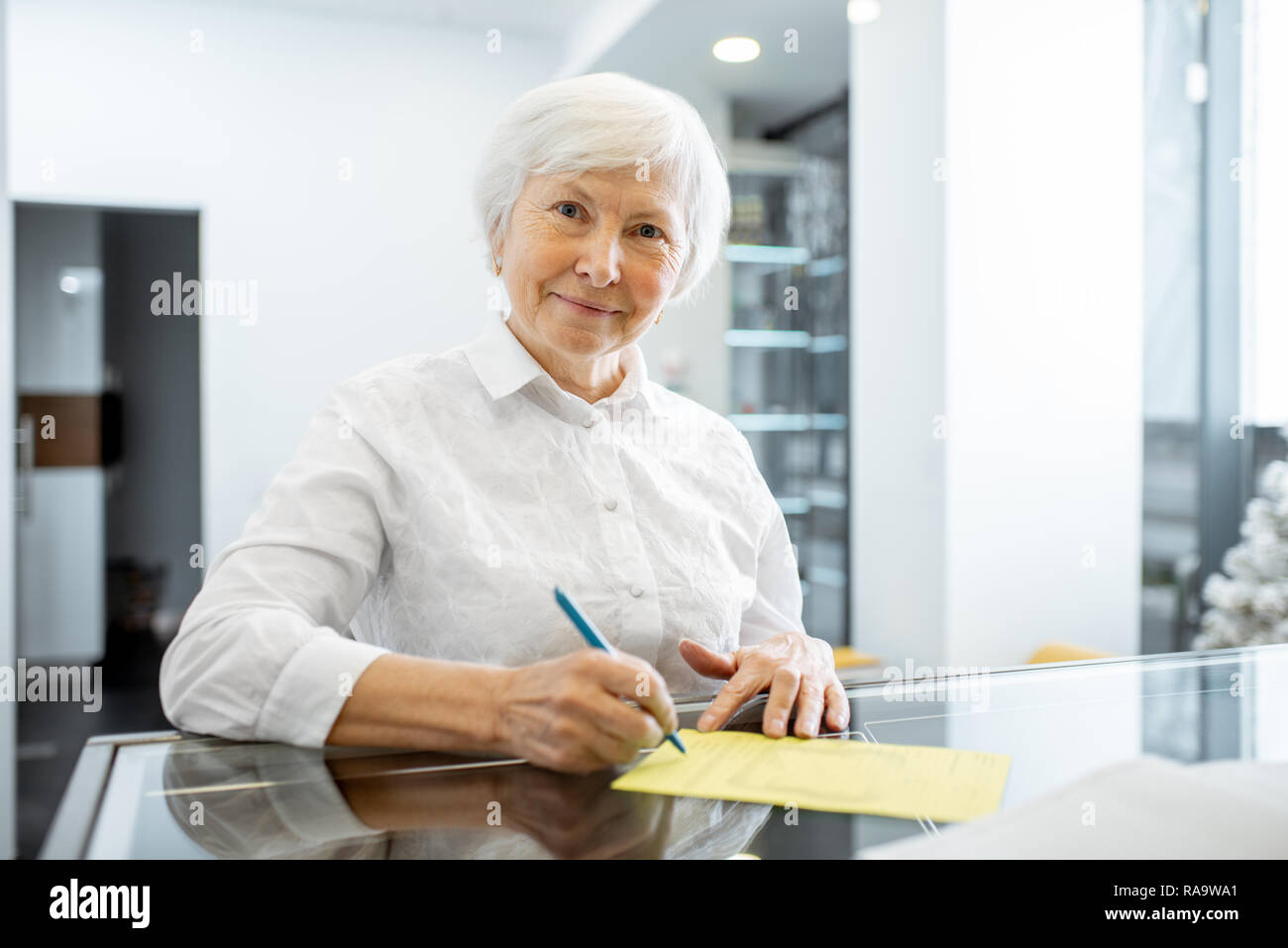 Beautiful senior woman signing some medical documents stannding at the hospital reception Stock Photo