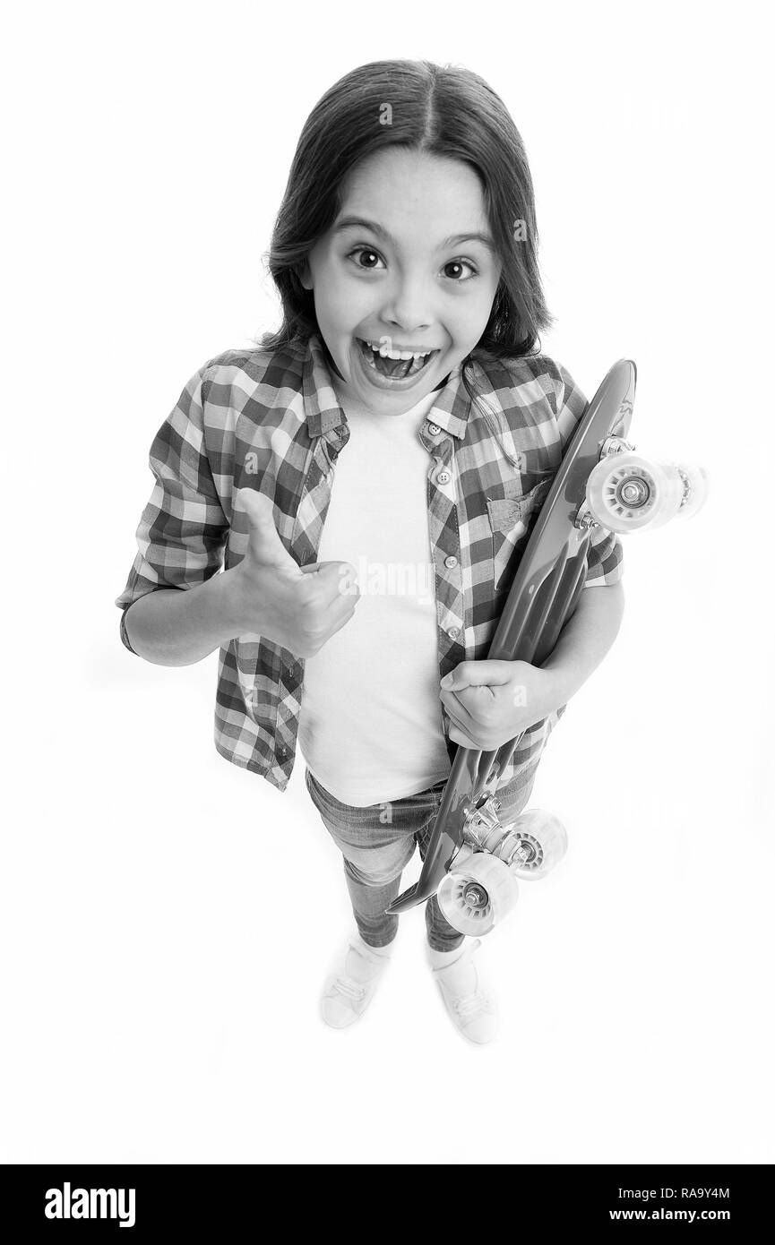 Joyful and happy. Kid girl casual style with penny board enjoy childhood. Girl joyful happy with skateboard isolated white. Hobby and leisure concept. Child likes skateboarding show thumb up gesture. Stock Photo