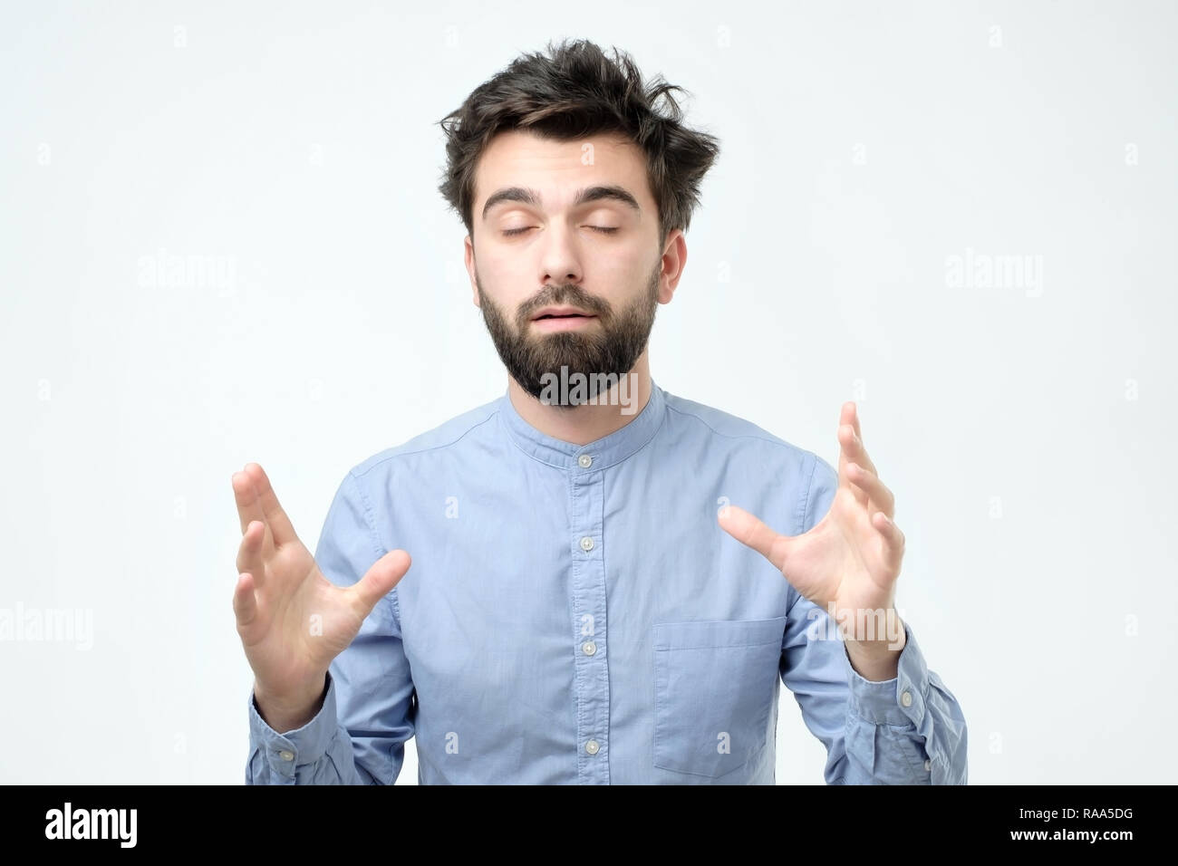 Unsatisfied sleepy guy with messy hair standing over gray background. Stock Photo