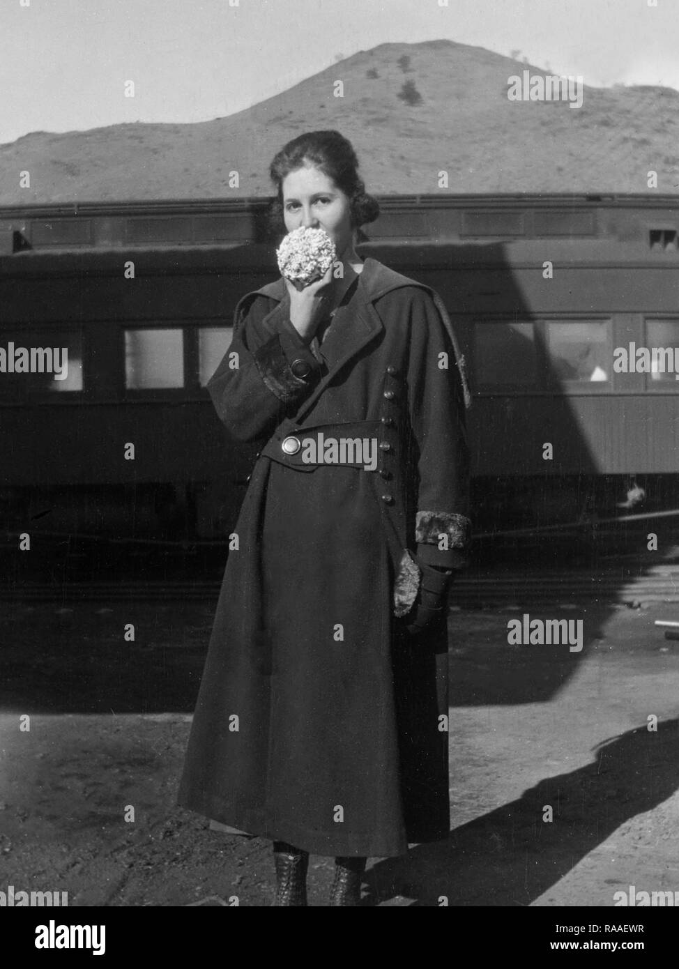 A young woman enjoys a popcorn ball on a Colorado train platform, ca. 1925. Stock Photo