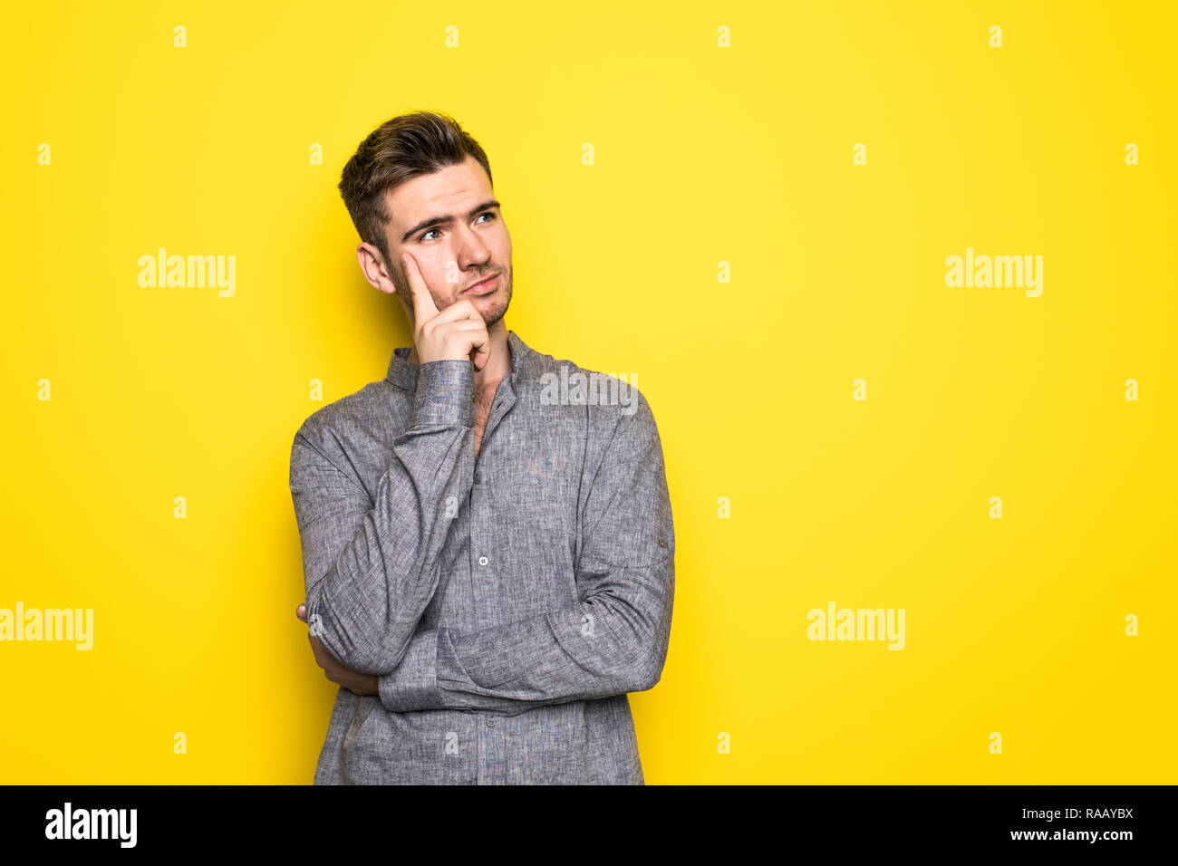 Portrait of thoughtful man who looks away touching his chin and weighs the pluses and minuses of the offer isolated on bright yellow background Stock Photo