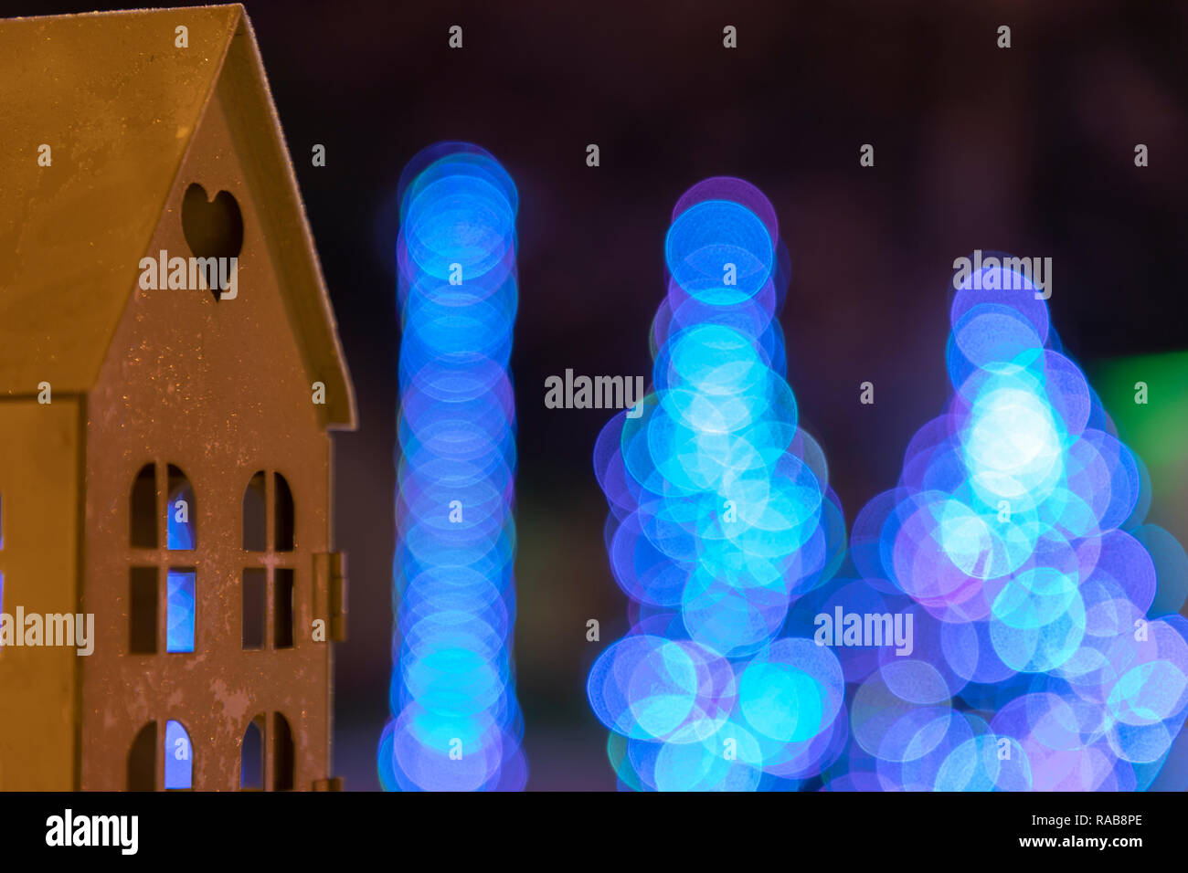 Small candle house on a table with christmas lights in the background