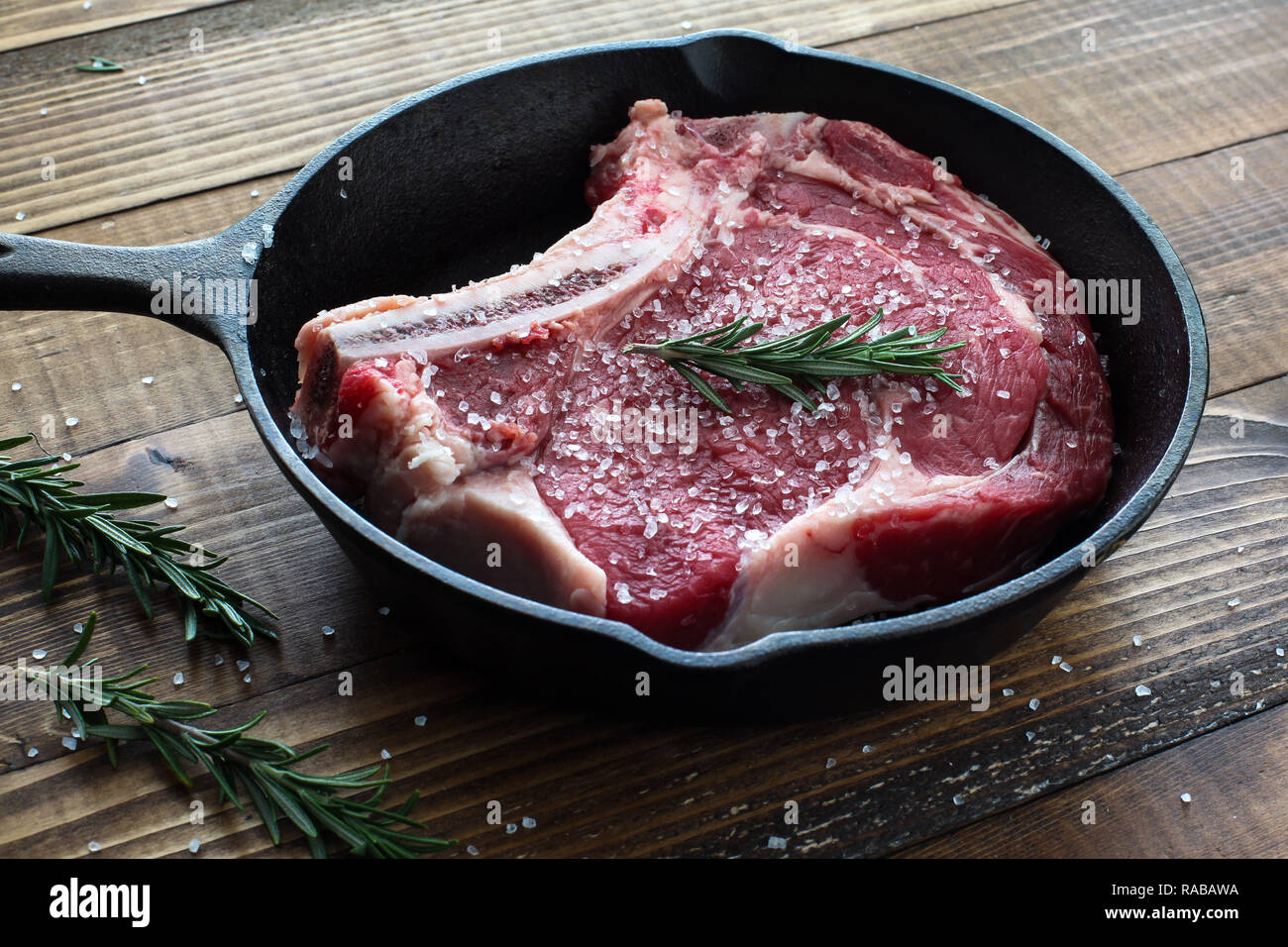 Beef steak bone in inside iron skillet with rosemary and sea salt Stock