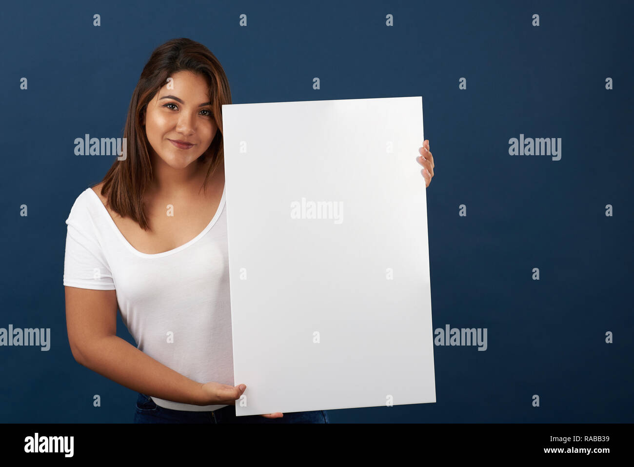 Pretty hispanic woman with white big banner isolated on blue studio background Stock Photo