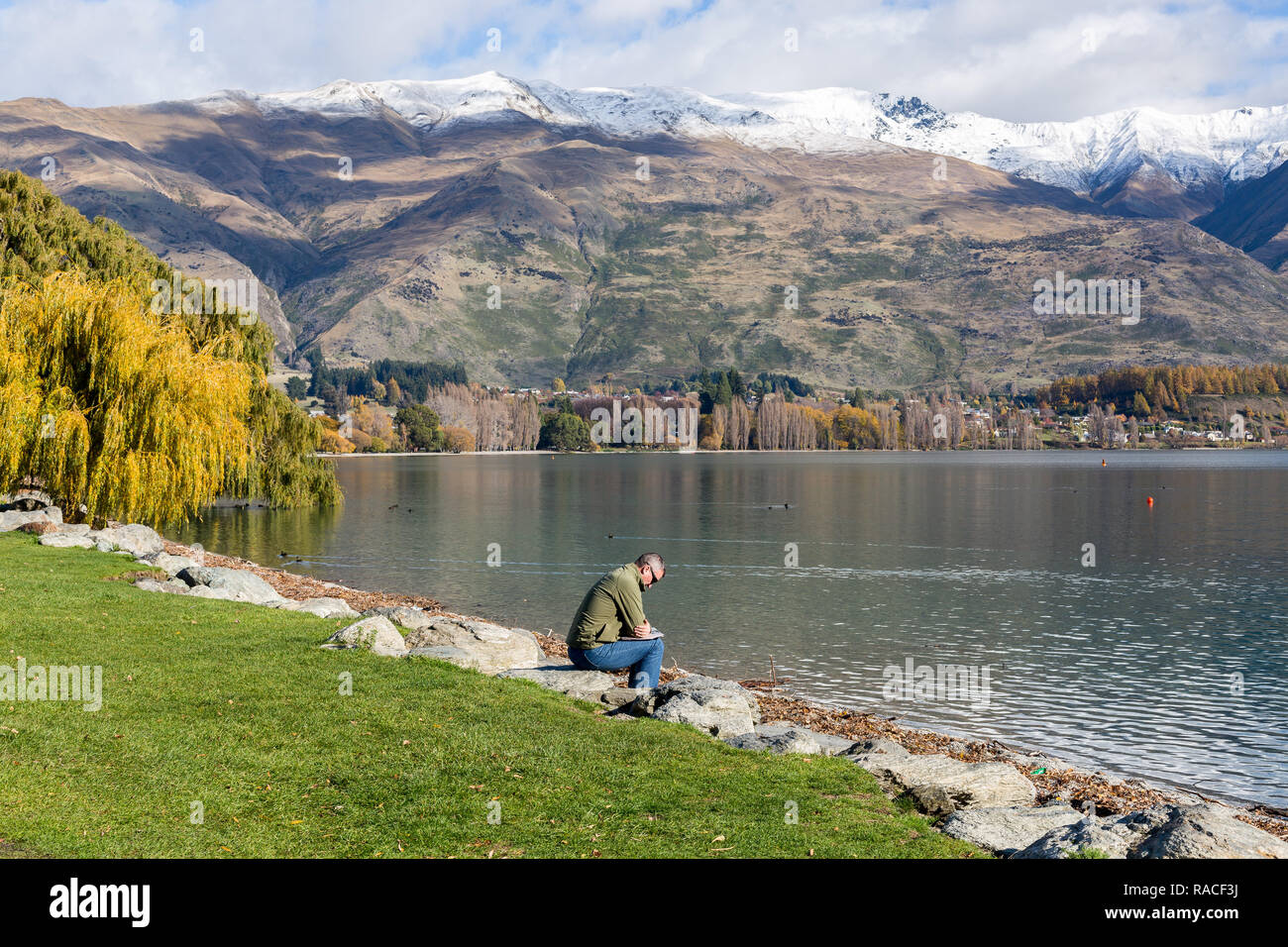 Man read paper sitting on rocks edge of Lake Wanaka Stock Photo