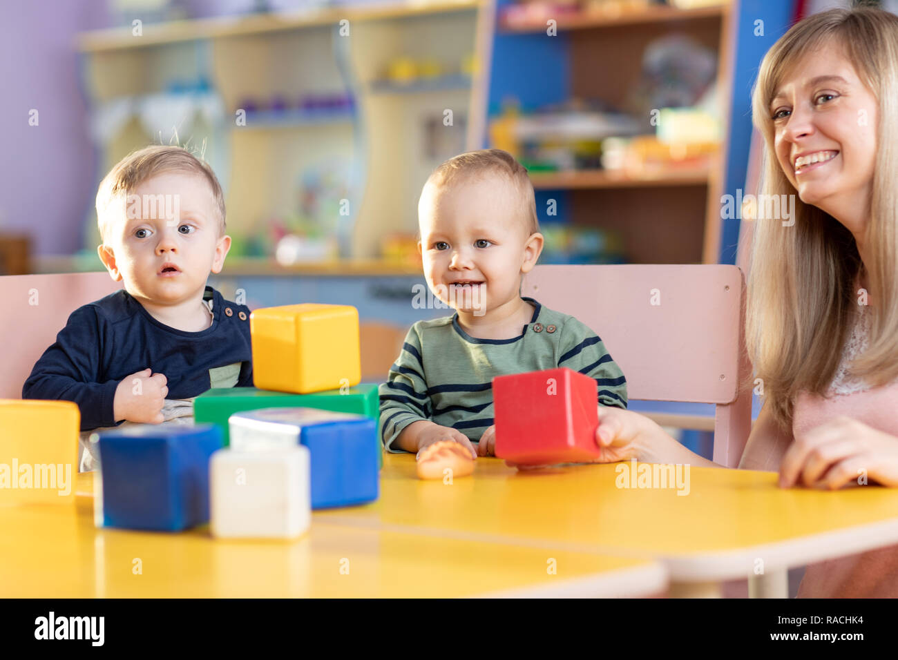 Cute woman and smiling kids playing educational toys at kindergarten or nursery room Stock Photo