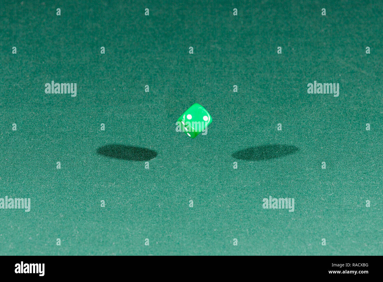 One green dice falling on a green table Stock Photo