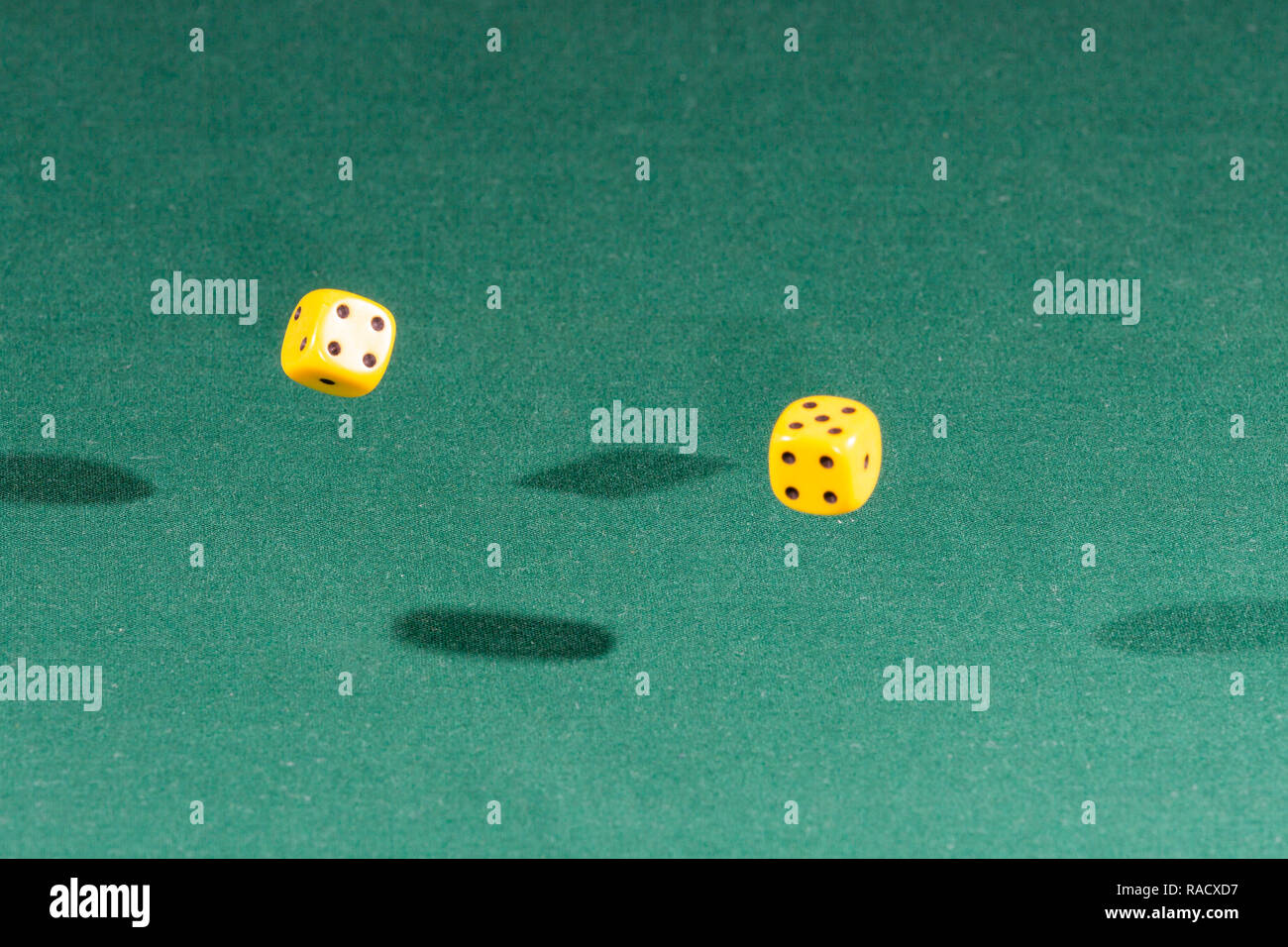 Two yellow dices falling on a green table Stock Photo