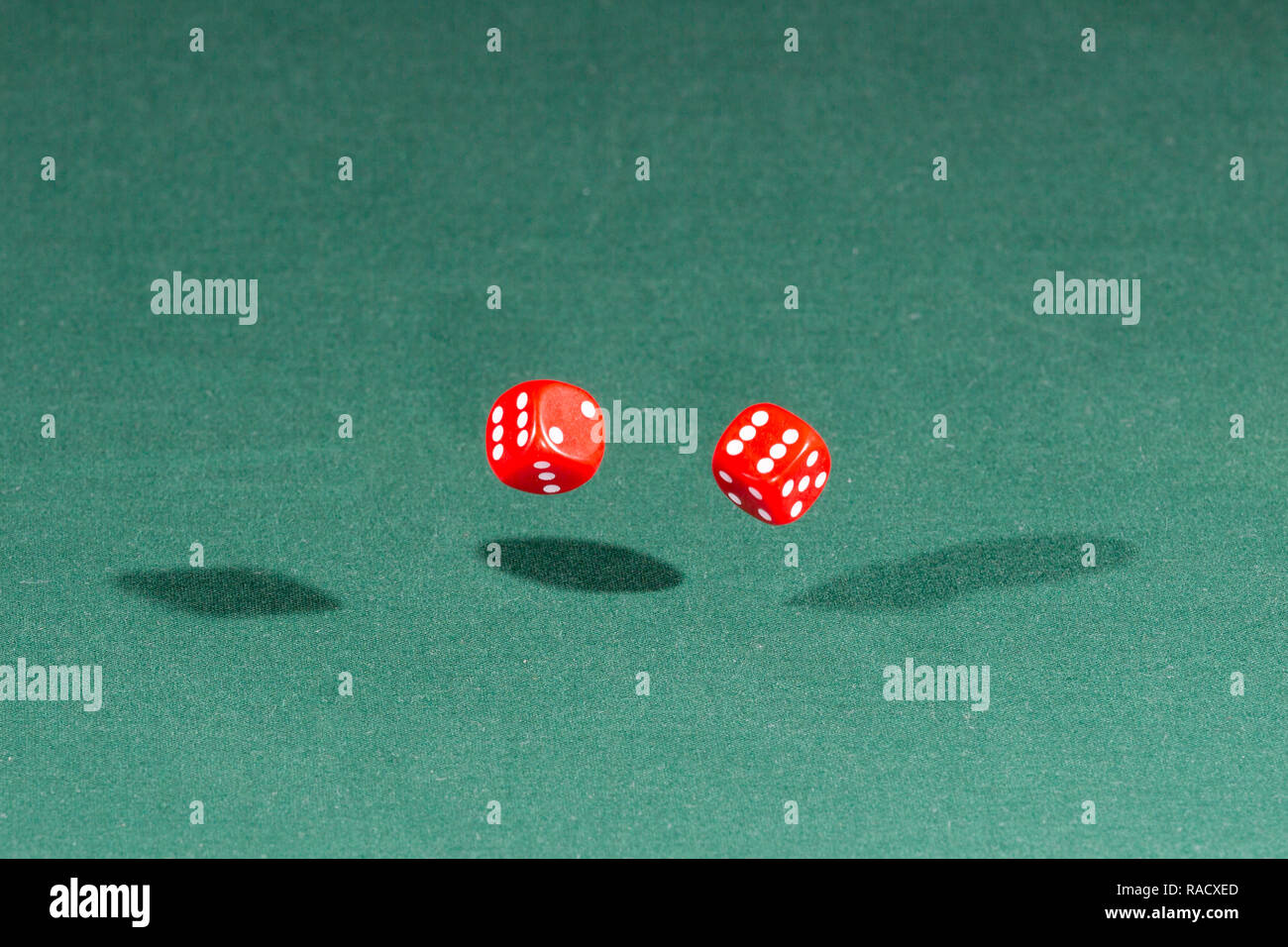 Two red dices falling on a green table Stock Photo