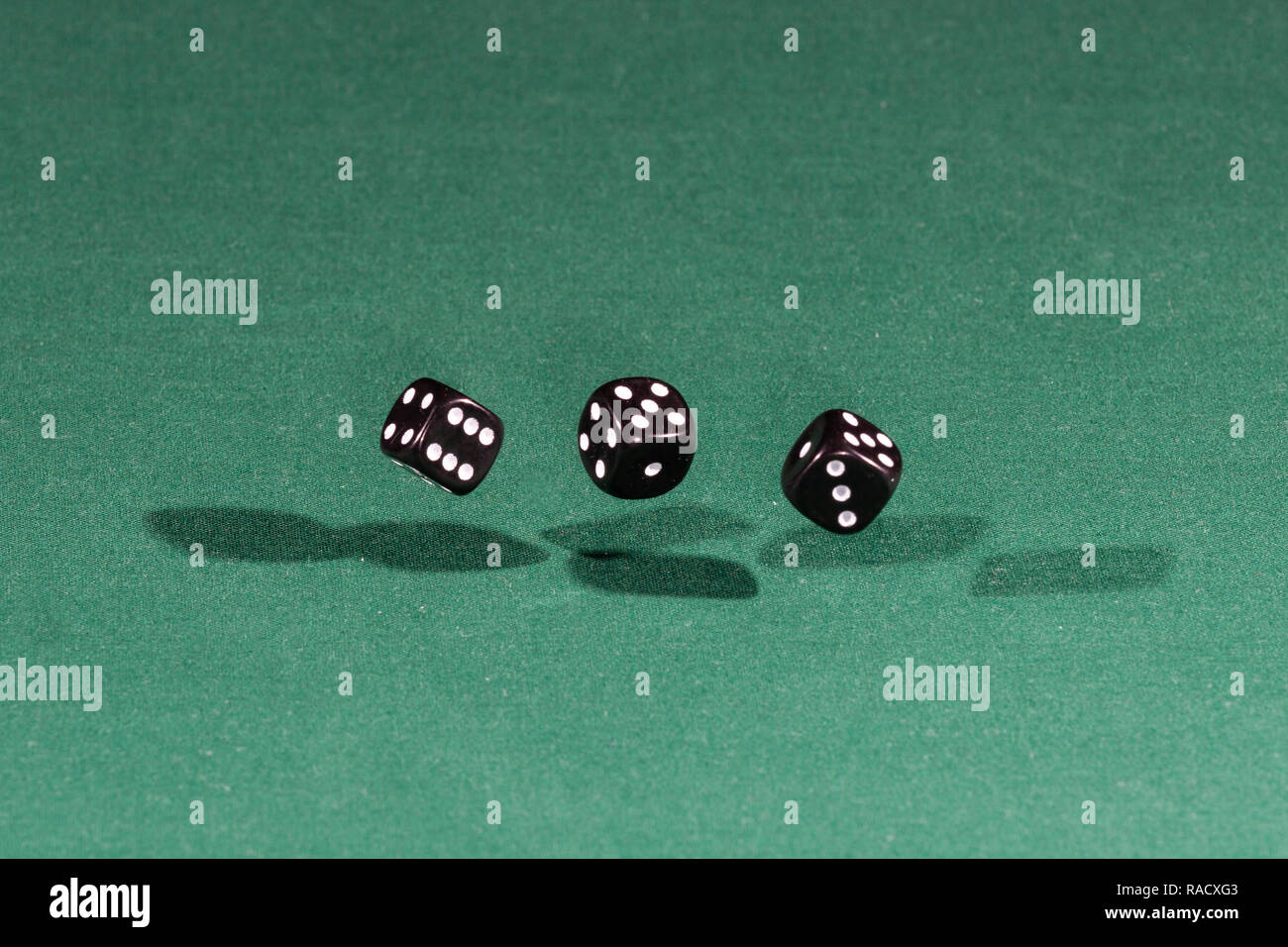 Three black dices falling on a green table Stock Photo