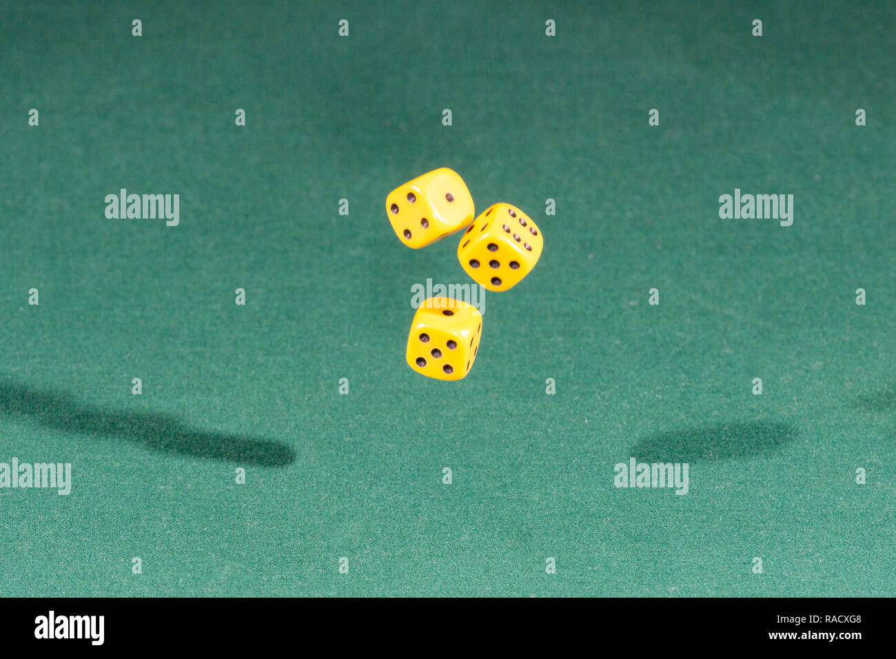 Three yellow dices falling on a green table Stock Photo