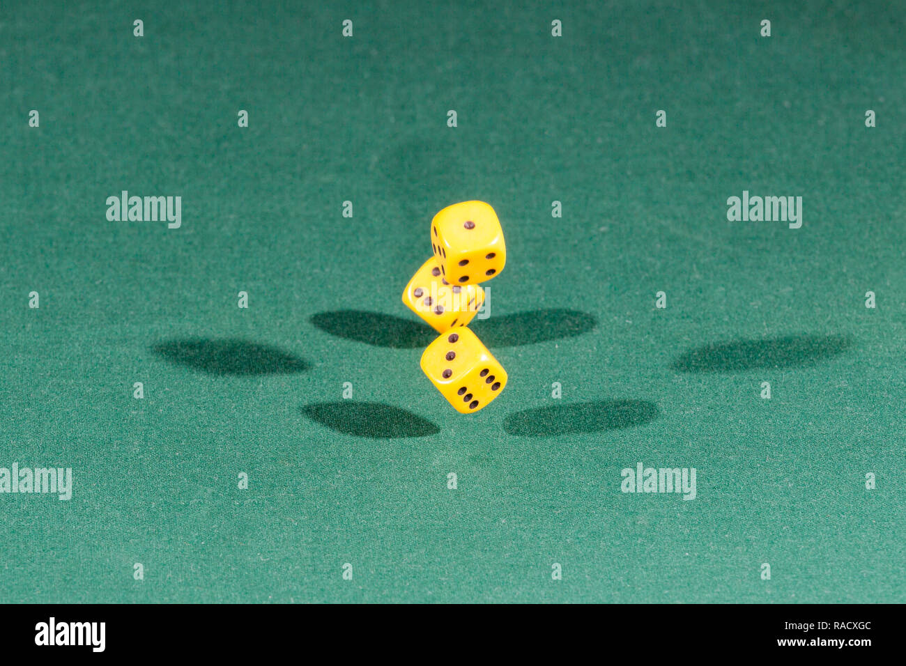 Three yellow dices falling on a green table Stock Photo
