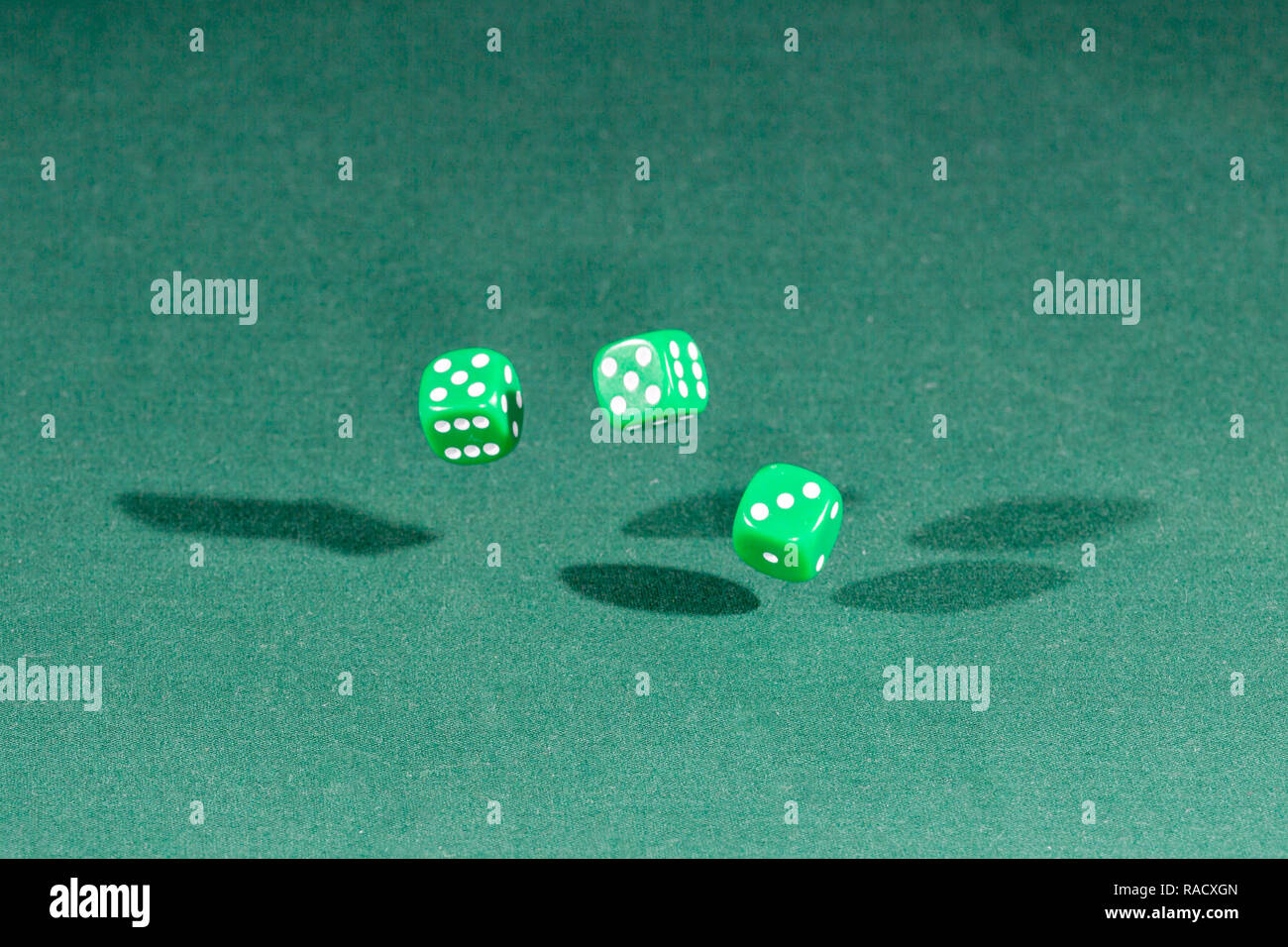 Three green dices falling on a green table Stock Photo